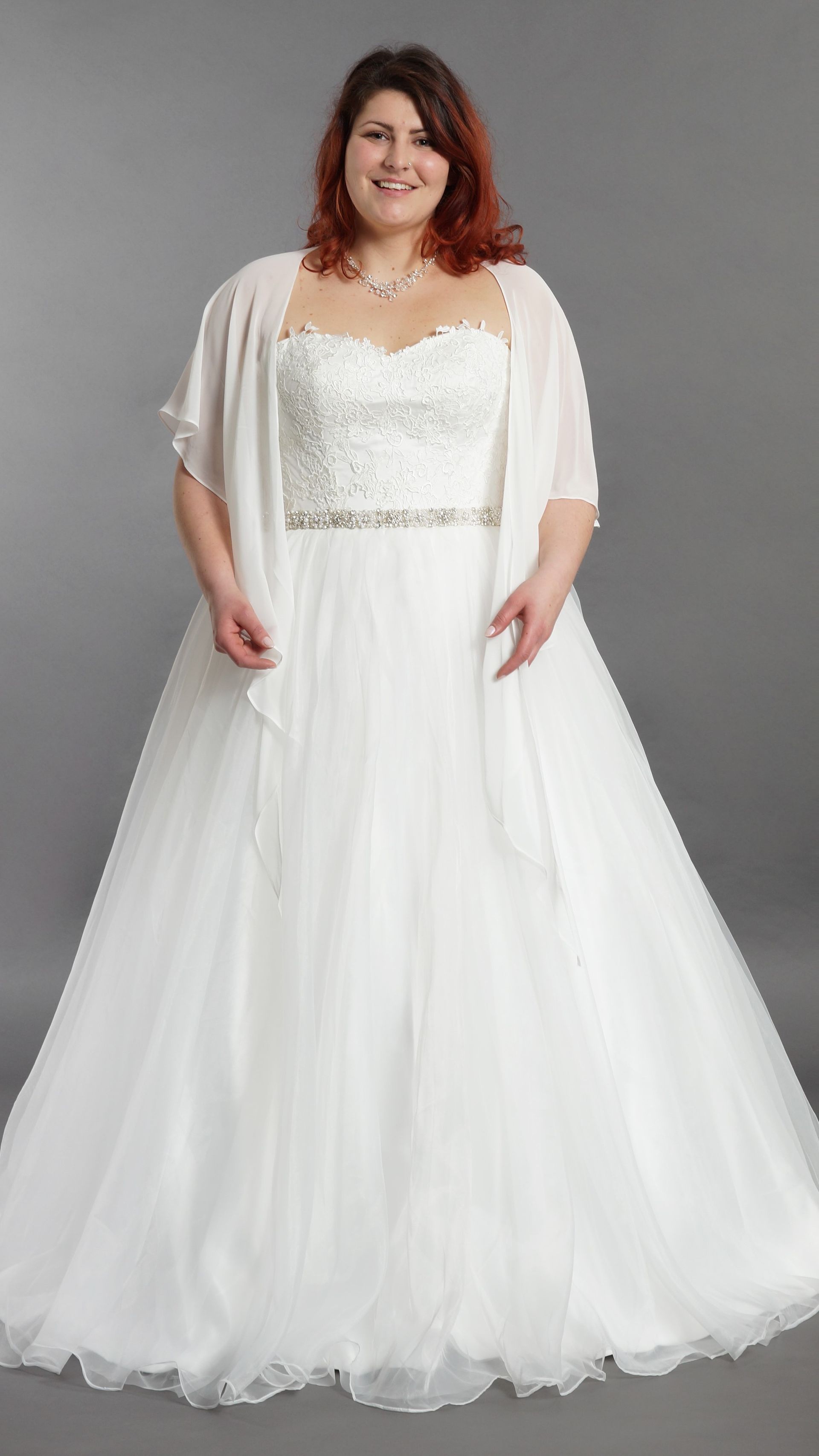 Eine Frau mit Übergröße trägt ein weißes Brautkleid und eine weiße Jacke.