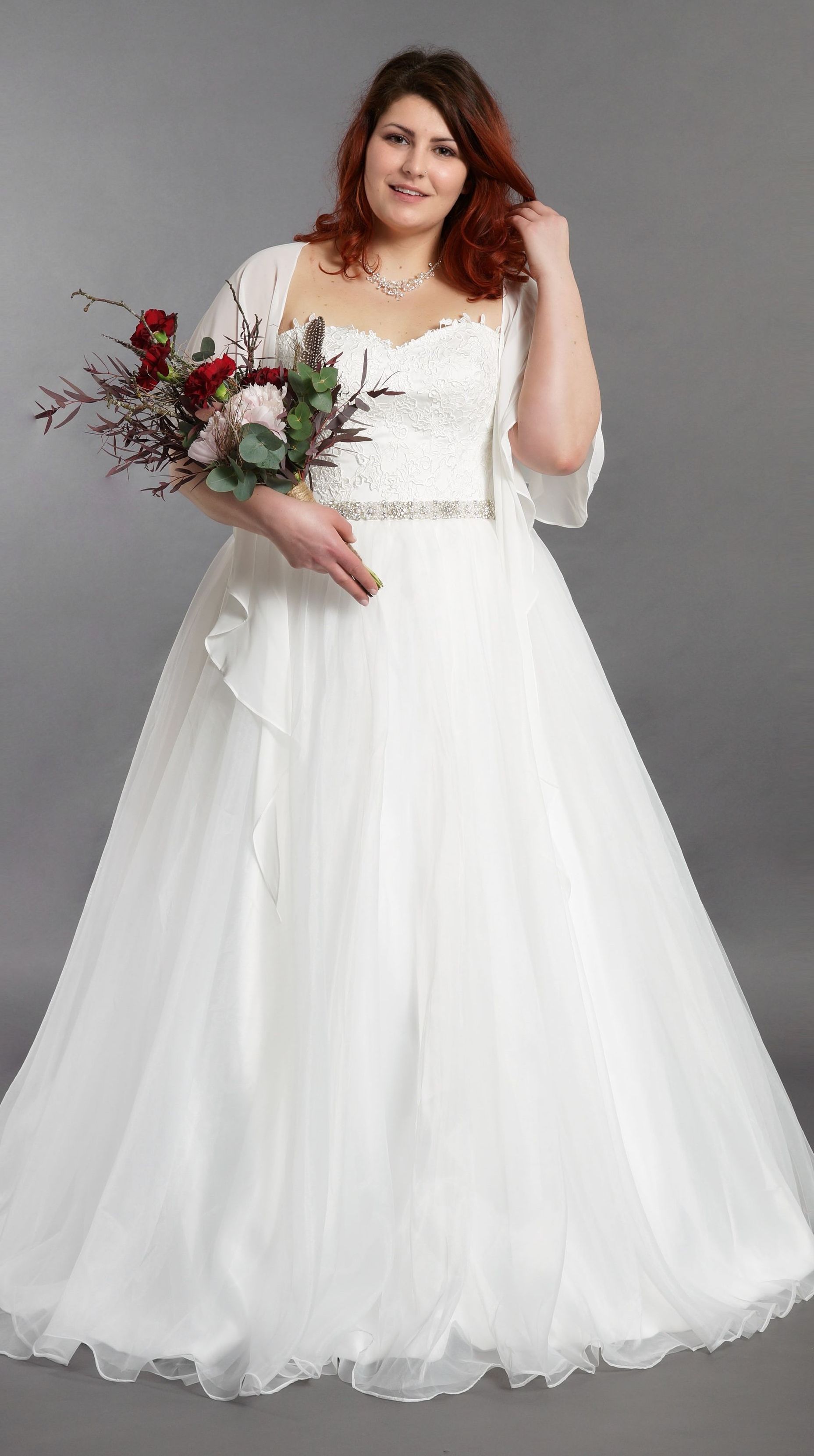 Eine Frau in einem weißen Brautkleid hält einen Blumenstrauß.