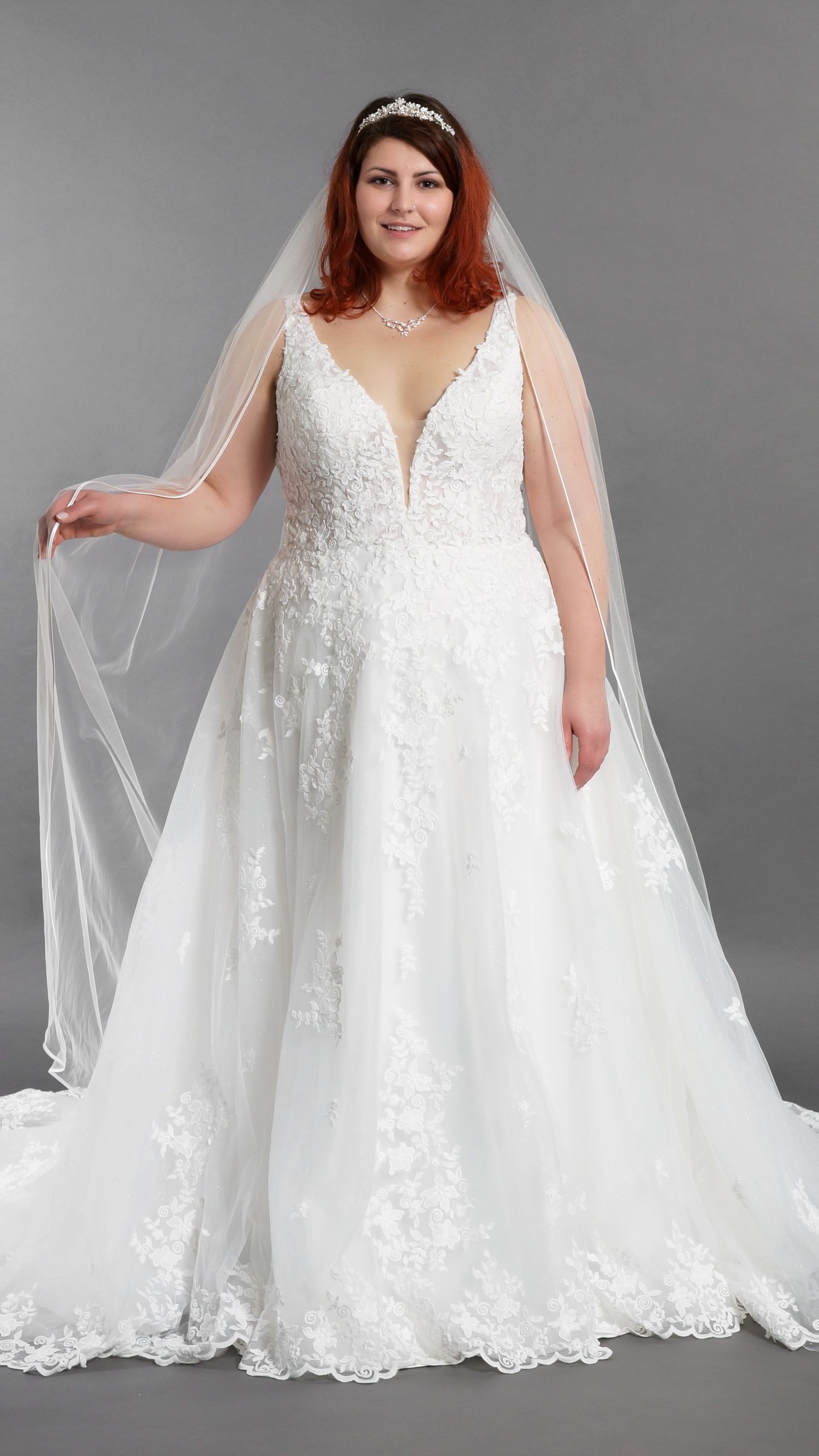 Eine Braut in Übergröße trägt ein weißes Brautkleid und einen Schleier.