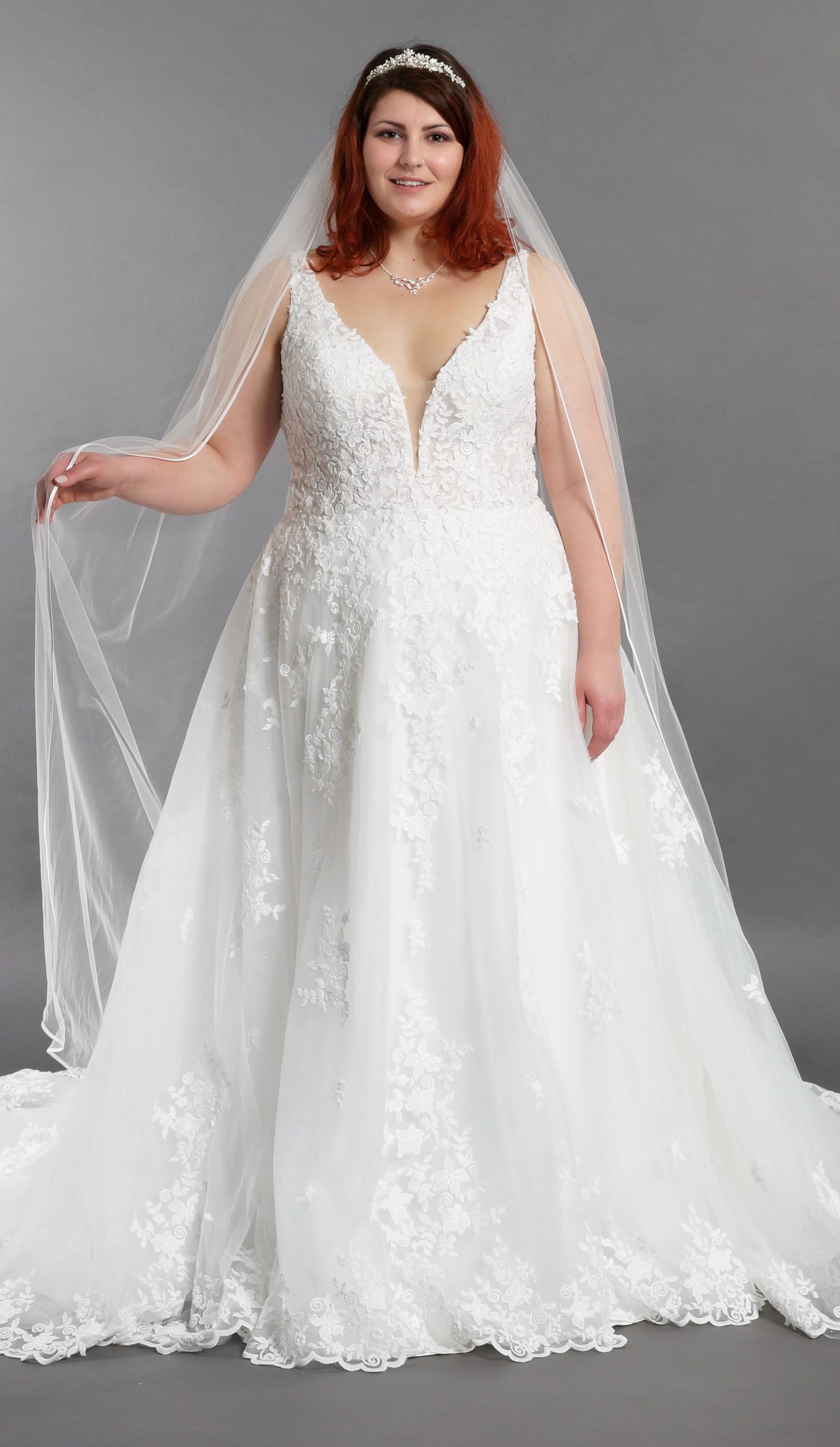 Eine Braut in Übergröße trägt ein weißes Brautkleid und einen Schleier.