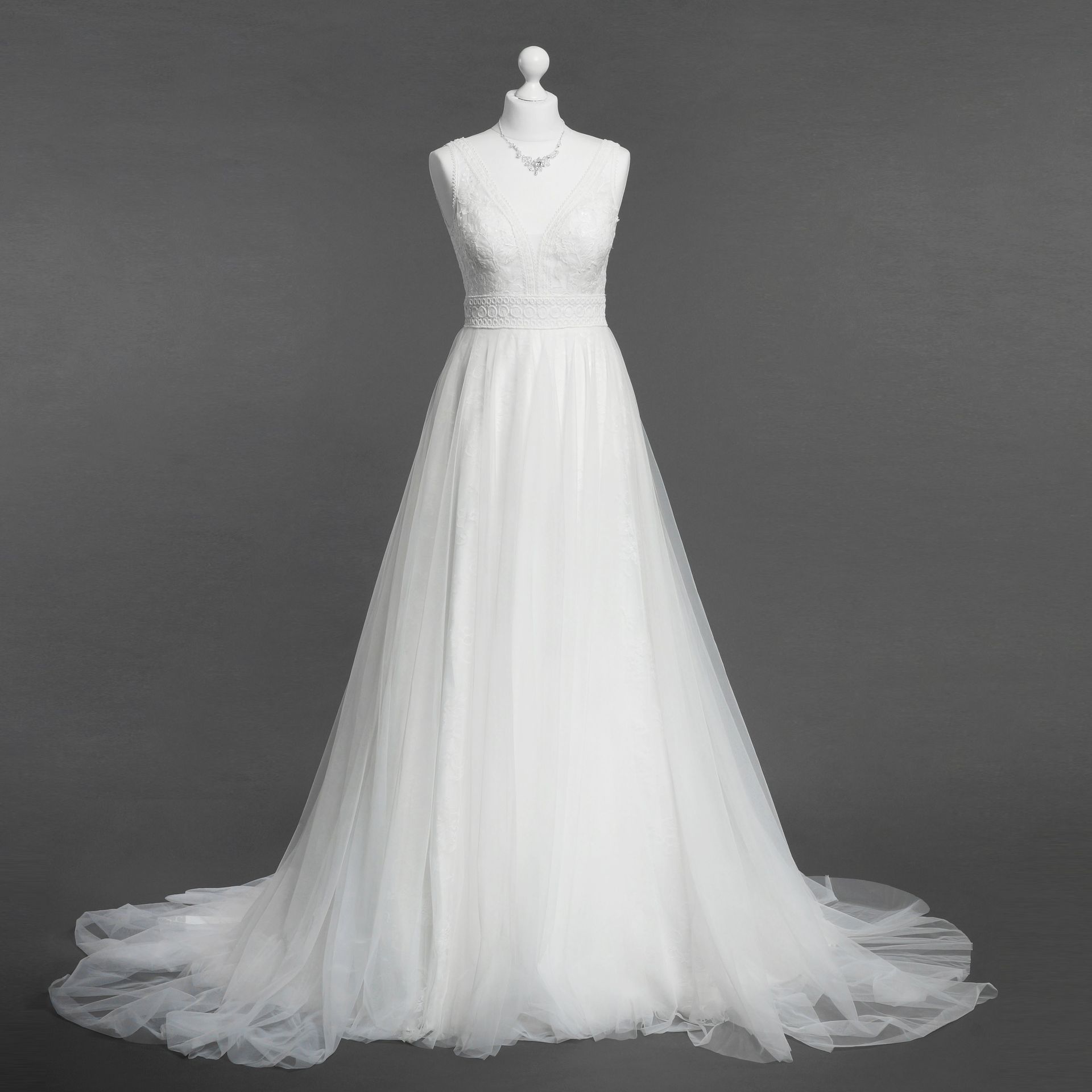 Auf einer Schaufensterpuppe hängt vor einem grauen Hintergrund ein weißes Brautkleid.