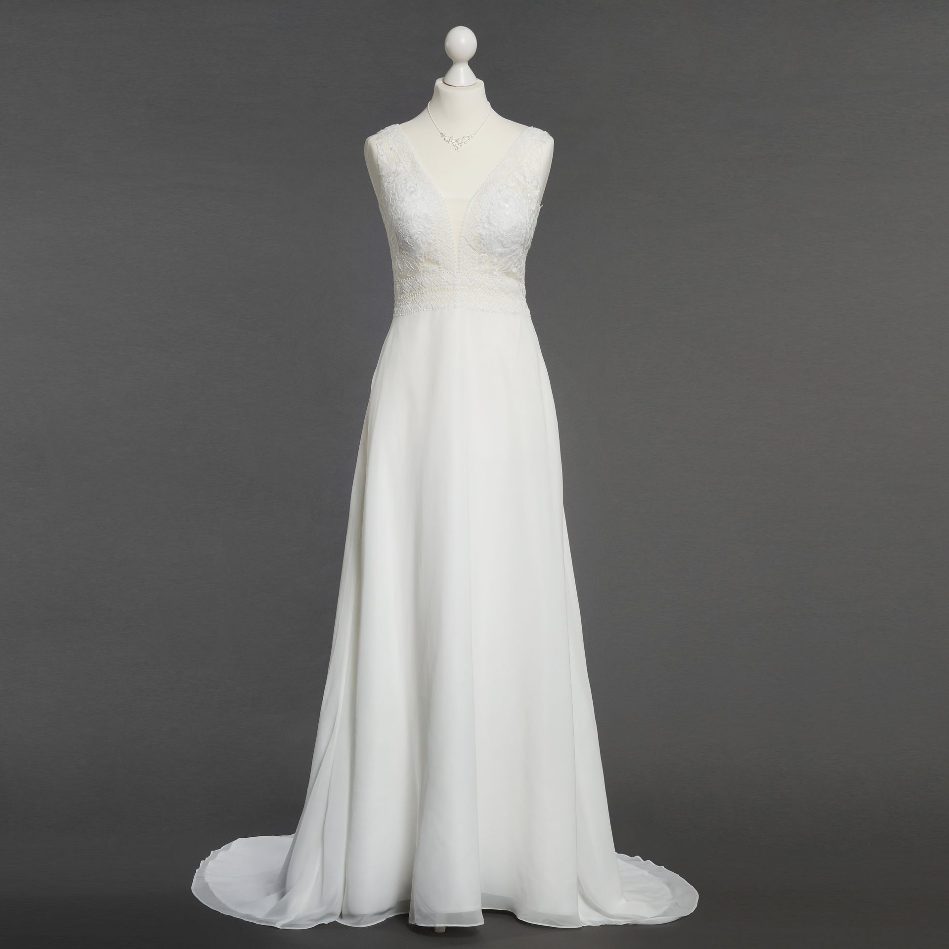 Ein weißes Brautkleid hängt auf einer Schaufensterpuppe vor einem grauen Hintergrund