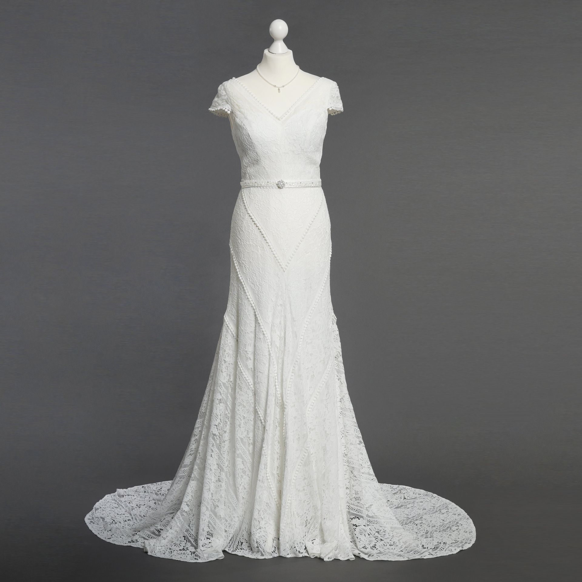 Ein weißes Spitzenbrautkleid hängt an einer Schaufensterpuppe