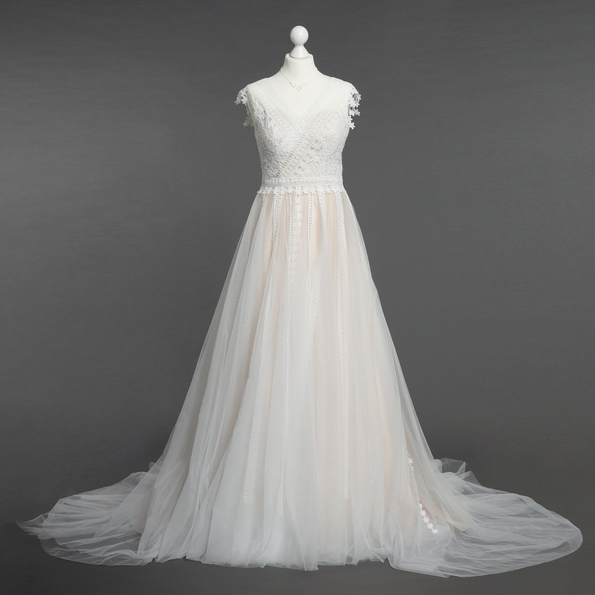 Auf einer Schaufensterpuppe hängt vor einem grauen Hintergrund ein weißes Brautkleid.