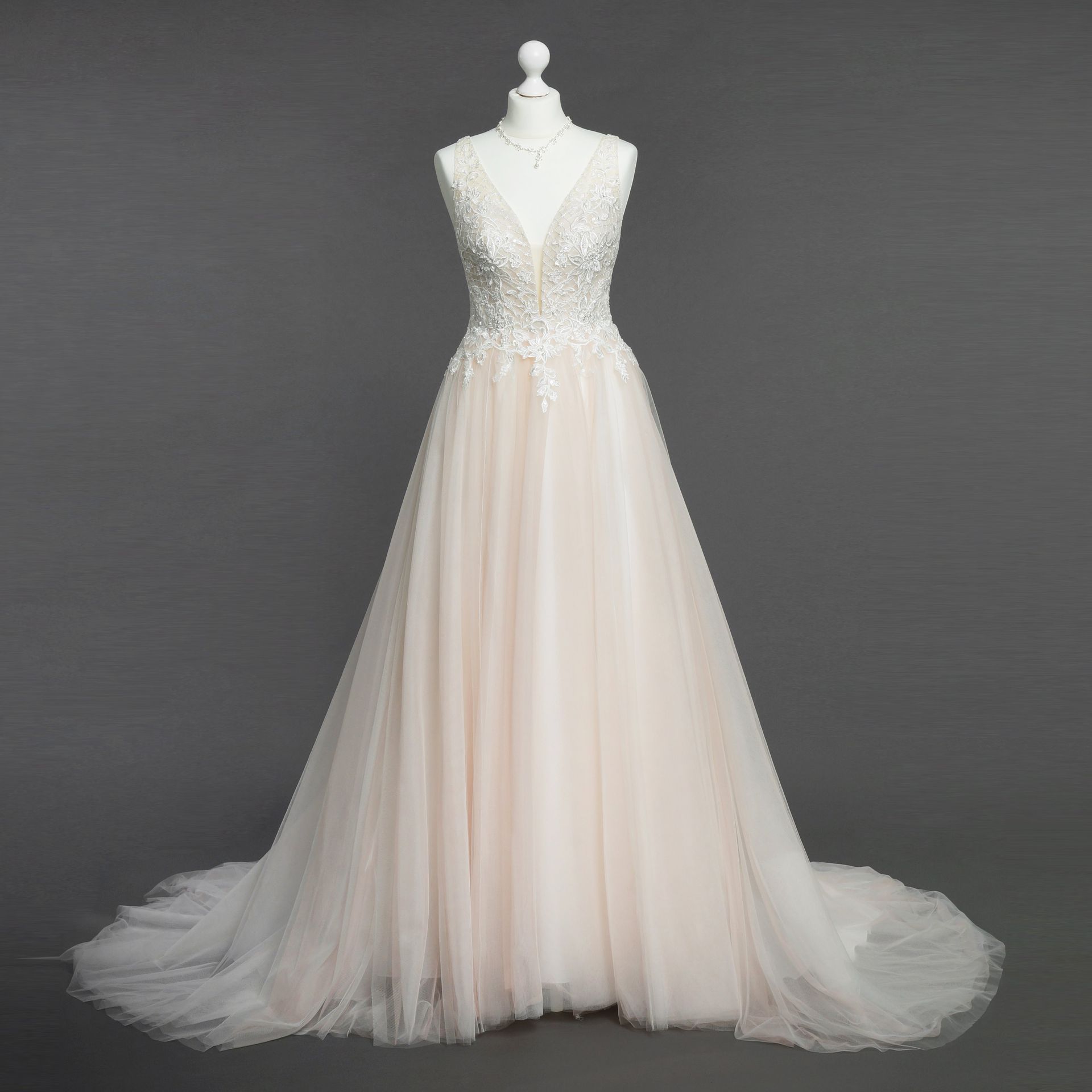 Auf einer Schaufensterpuppe hängt ein weißes Brautkleid vor einem grauen Hintergrund.