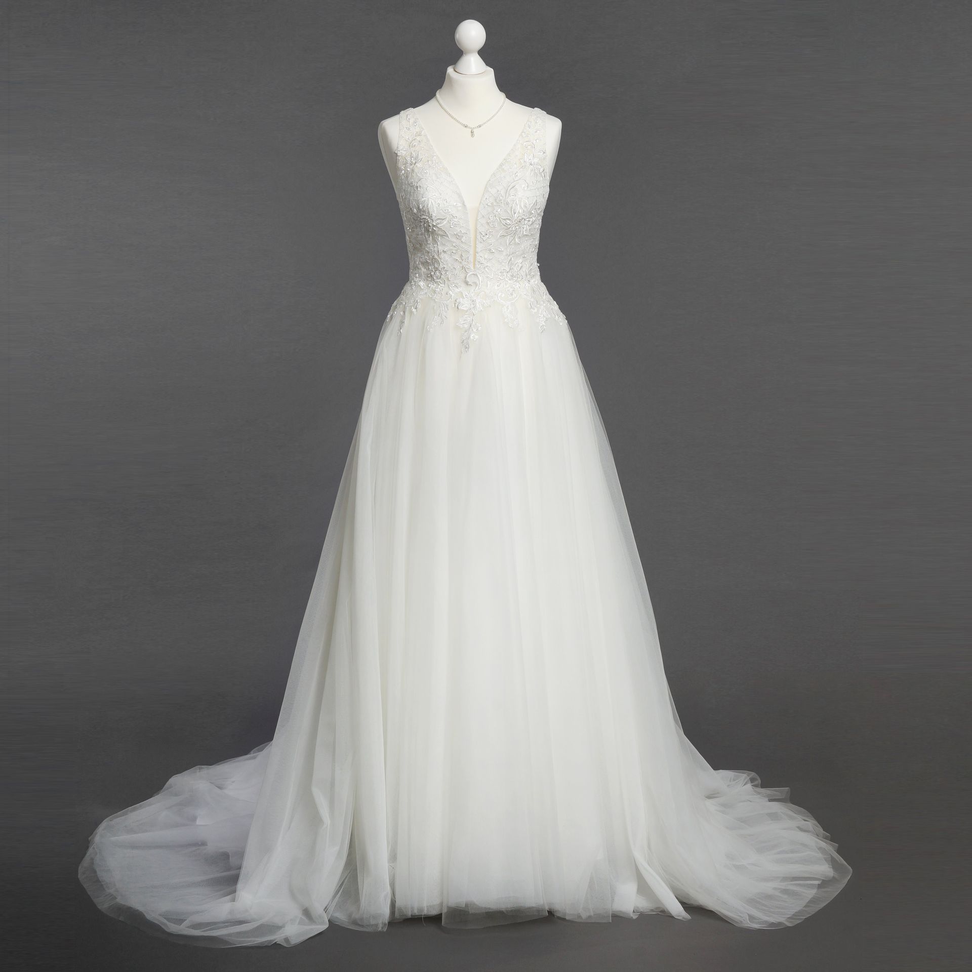 Auf einer Schaufensterpuppe hängt vor einem grauen Hintergrund ein weißes Brautkleid.