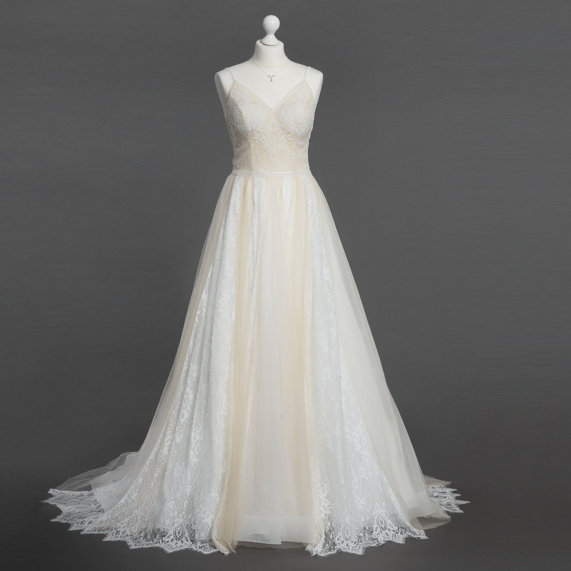 Ein weißes Spitzenbrautkleid hängt an einer Schaufensterpuppe