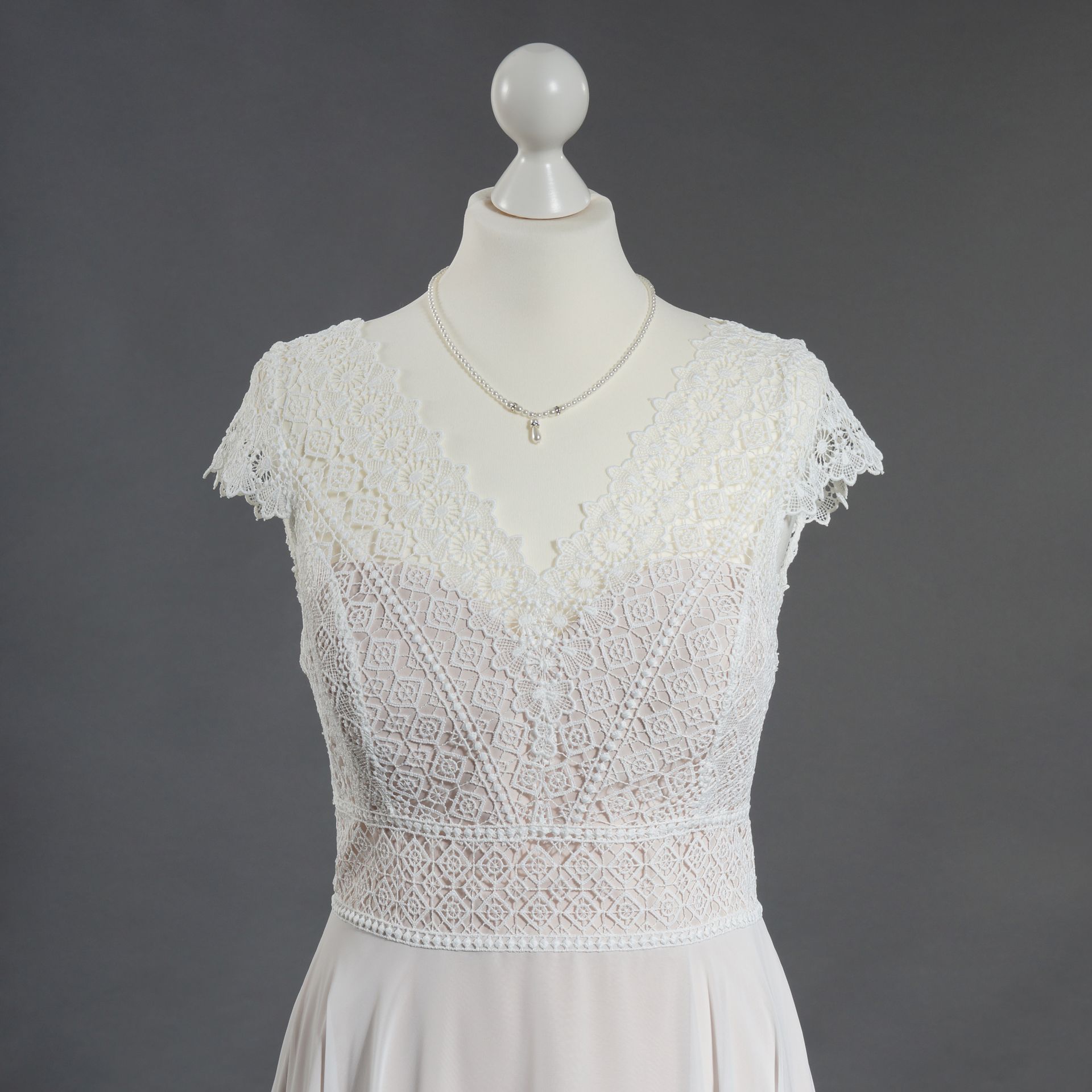 Ein weißes Spitzenkleid hängt an einer Schaufensterpuppe mit einer Halskette