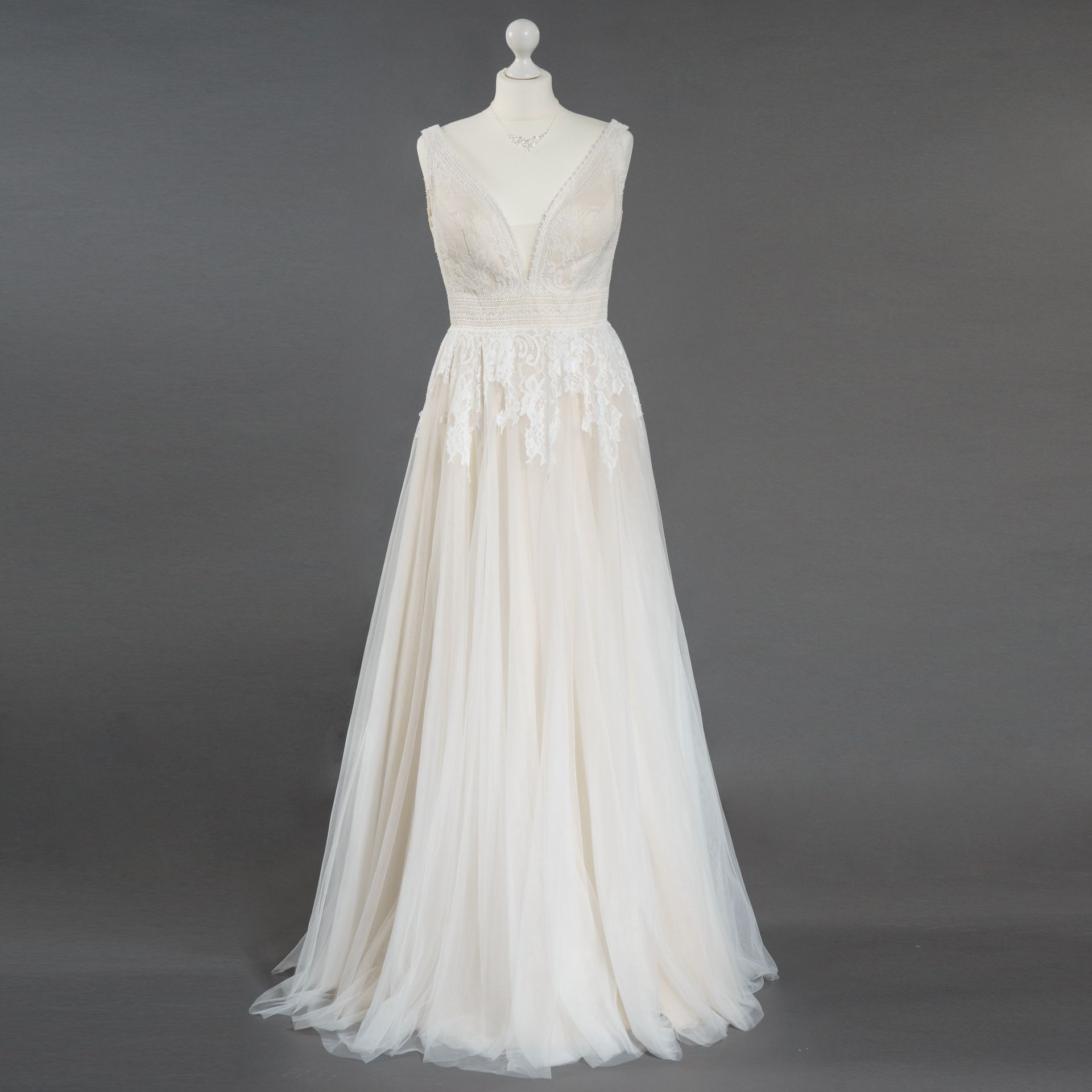 Ein weißes Brautkleid hängt auf einer Schaufensterpuppe vor einem grauen Hintergrund