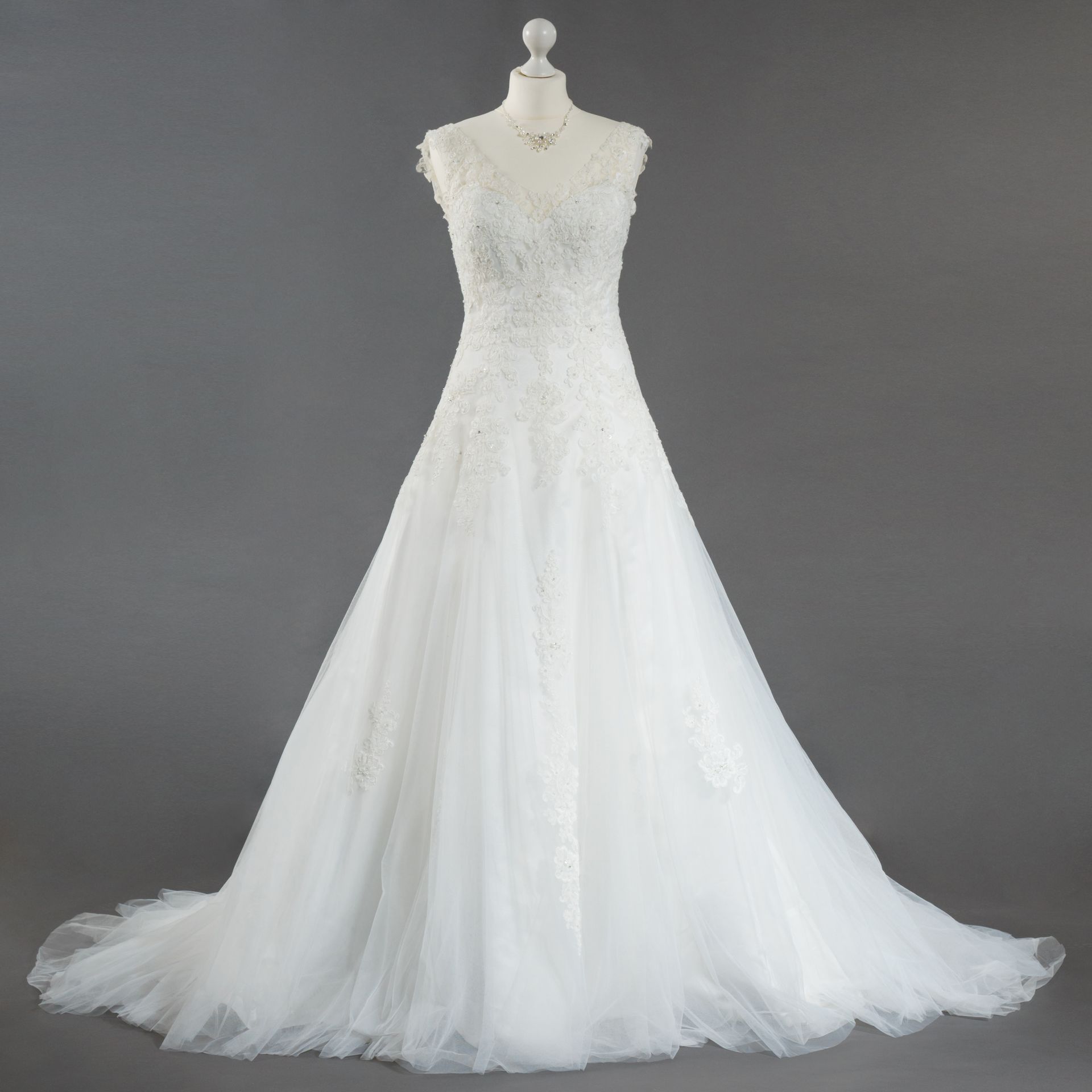 Ein weißes Brautkleid hängt auf einer Schaufensterpuppe vor einem grauen Hintergrund