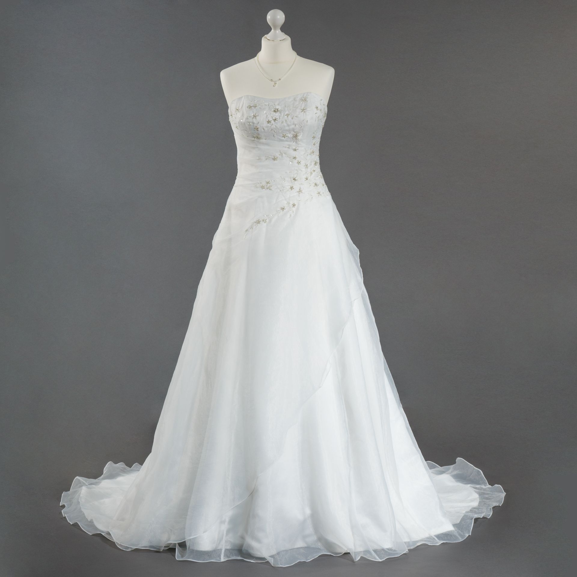 Ein weißes Brautkleid liegt auf einer Schaufensterpuppe mit grauem Hintergrund