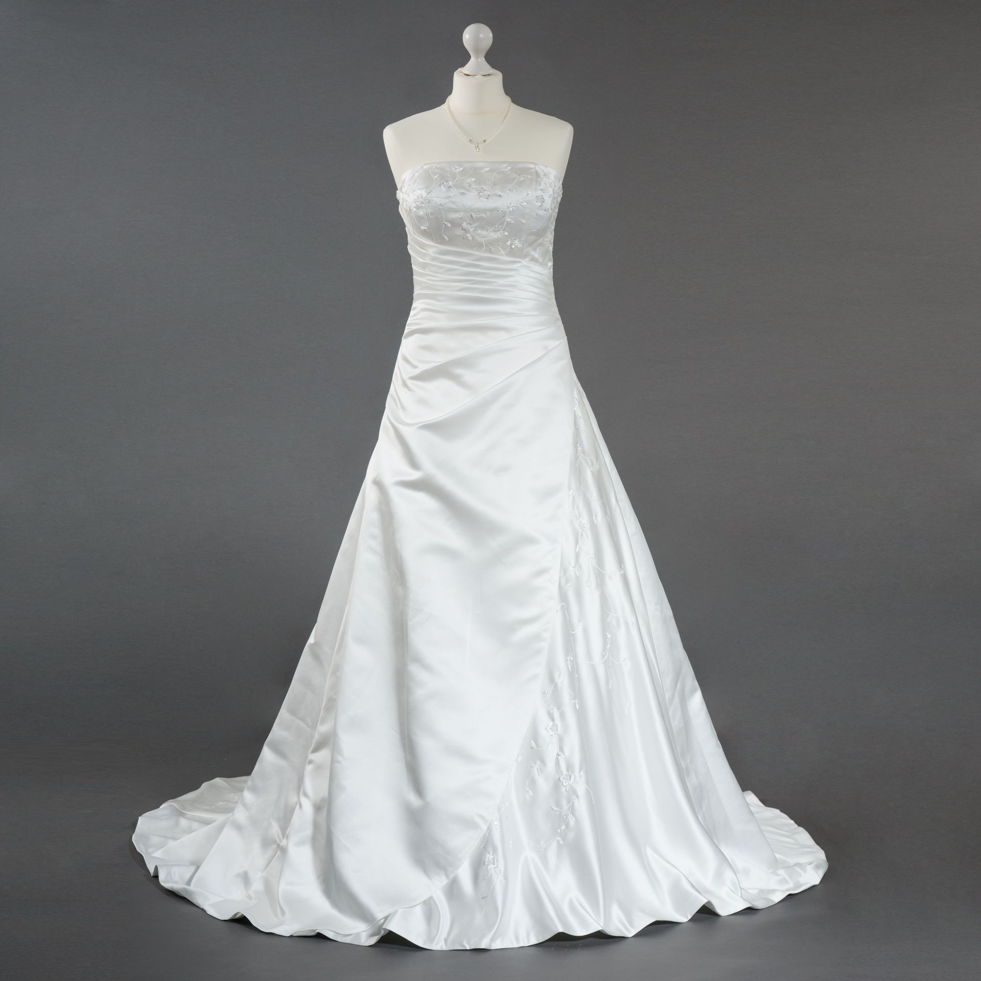 Ein weißes trägerloses Brautkleid hängt an einer Schaufensterpuppe