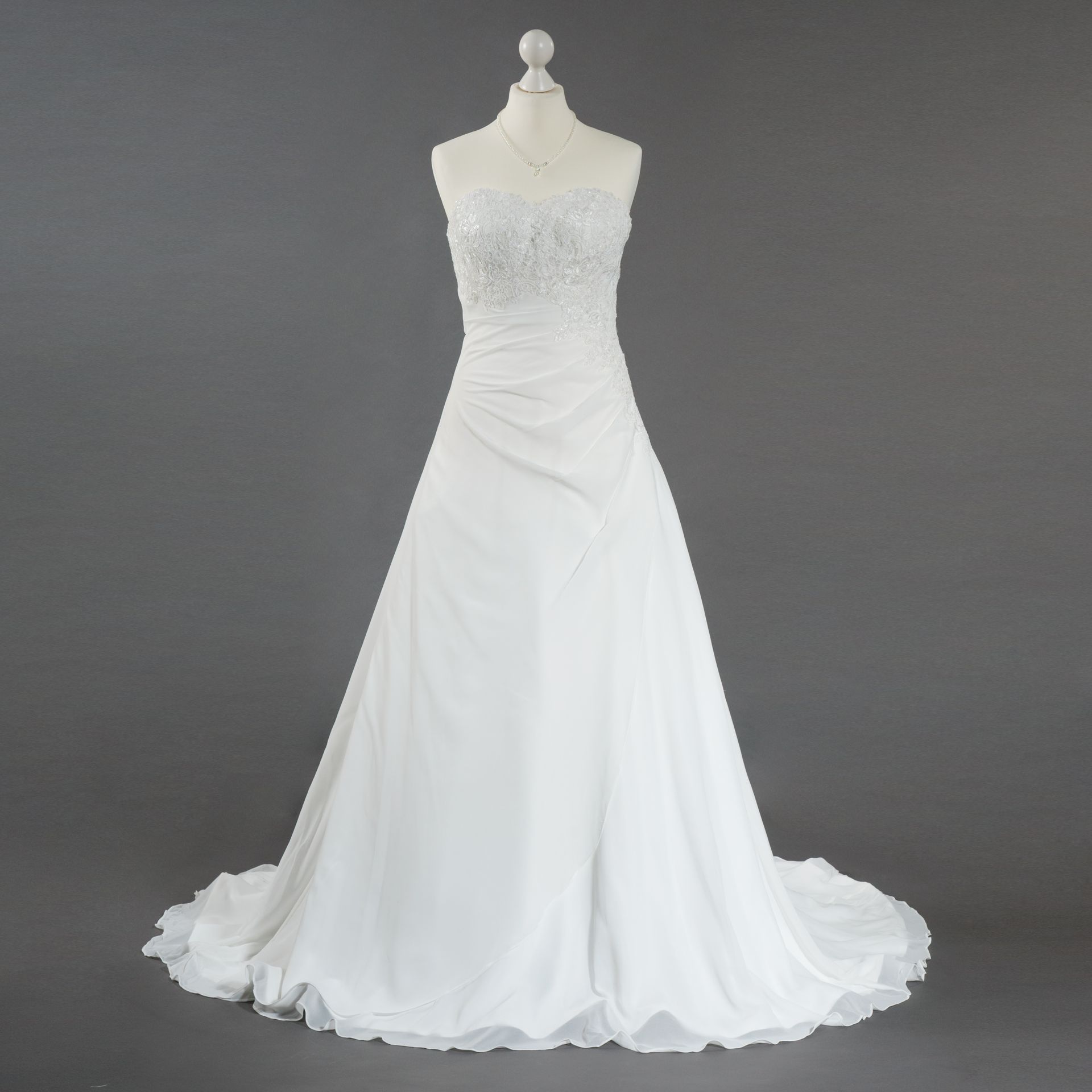 Ein weißes trägerloses Brautkleid hängt an einer Schaufensterpuppe