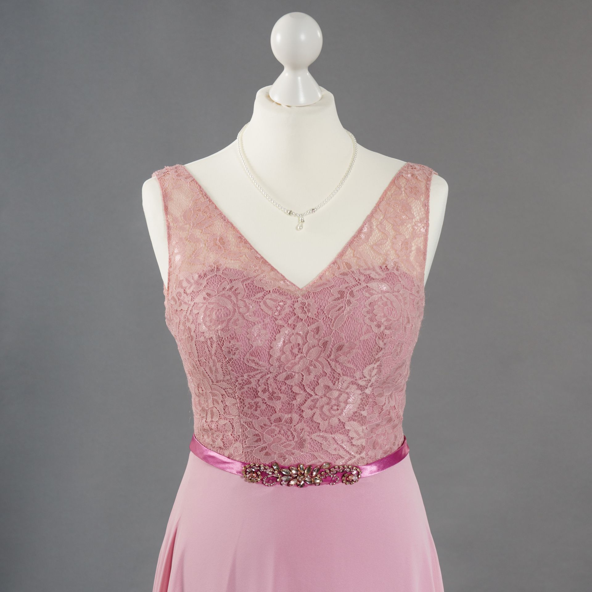 Ein rosa Spitzenkleid ist auf einer Schaufensterpuppe mit einer Halskette