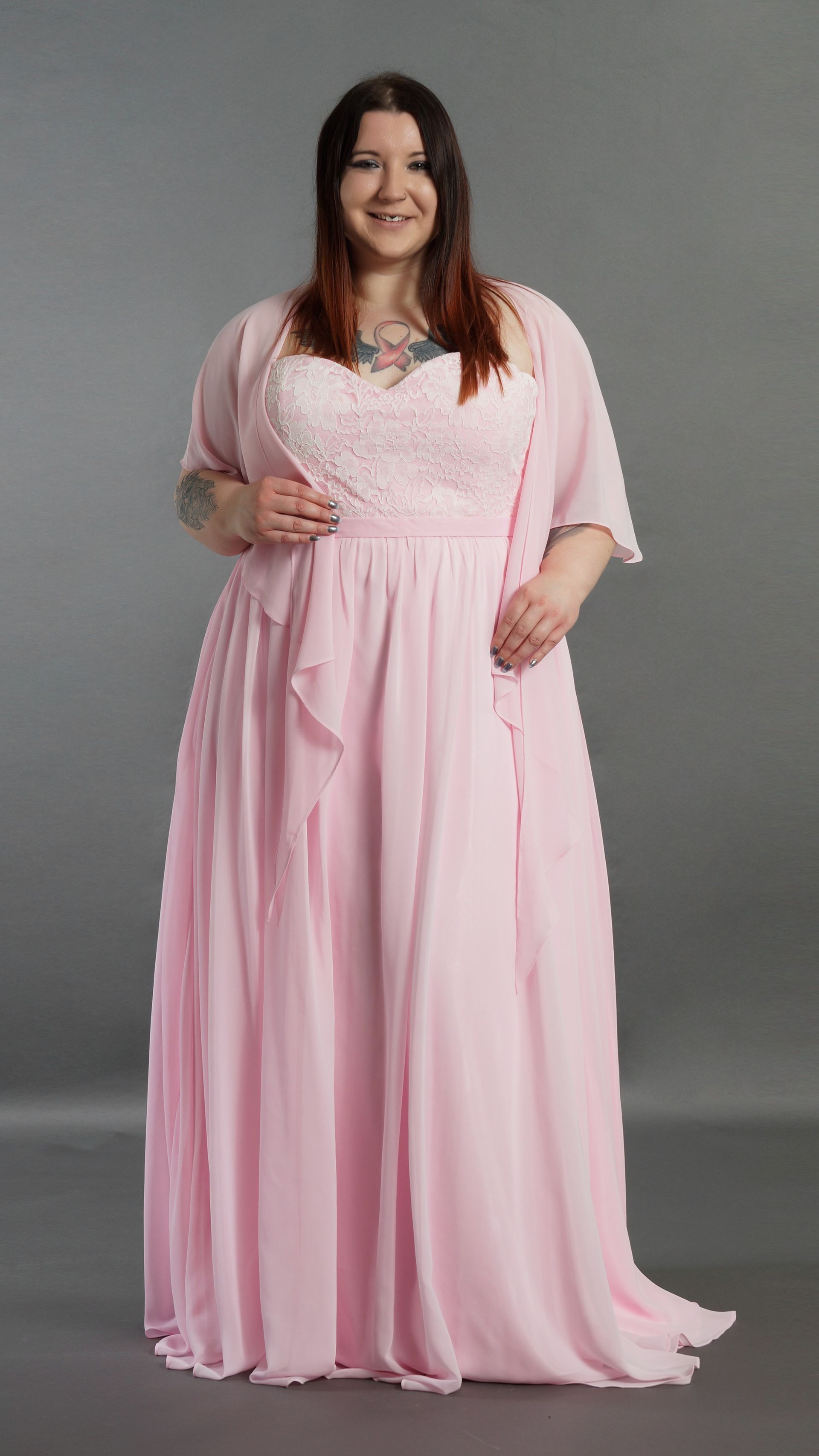 Eine Frau mit Übergröße trägt ein rosa Kleid und eine rosa Jacke.