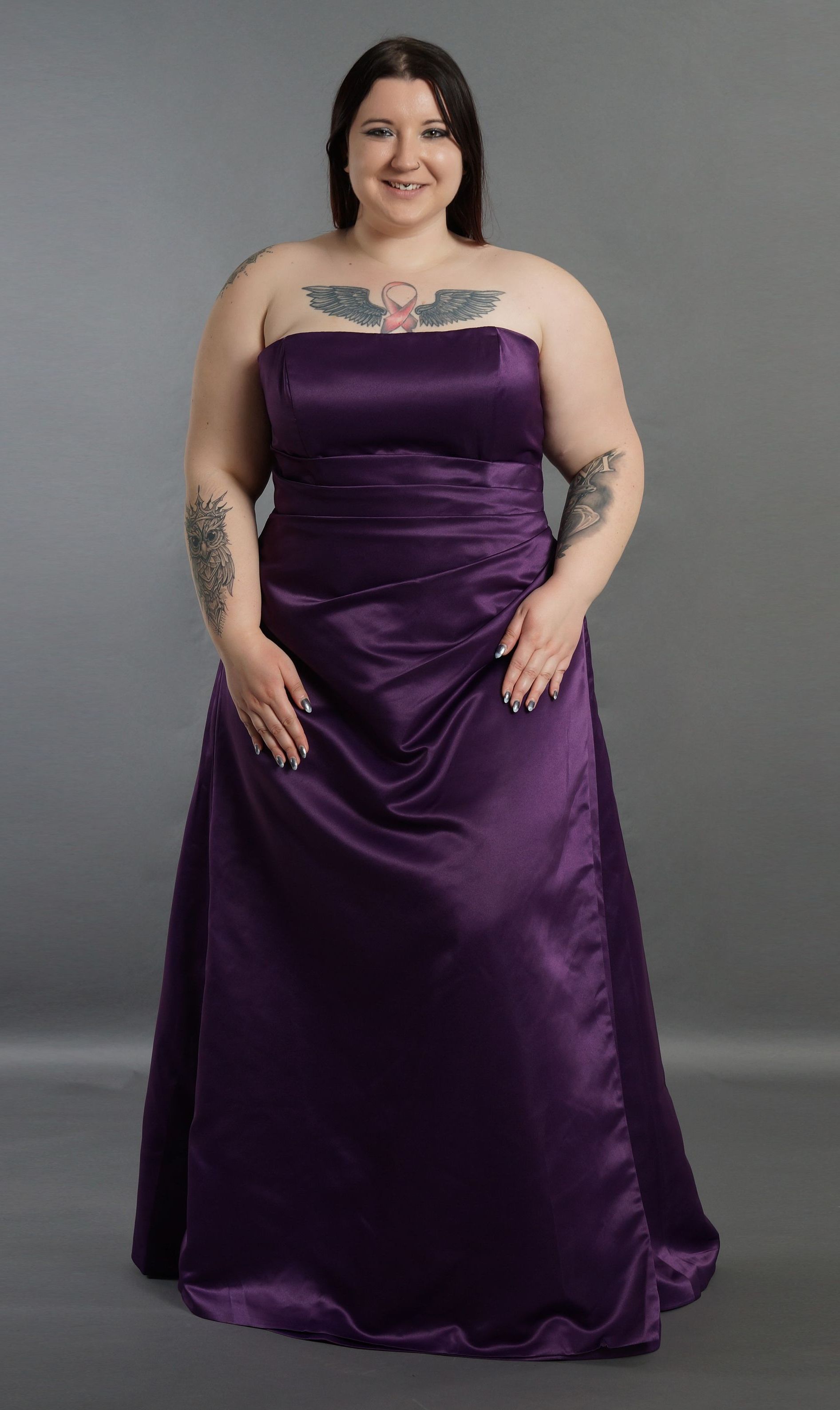 Eine Frau mit Tattoos trägt ein lila trägerloses Kleid.