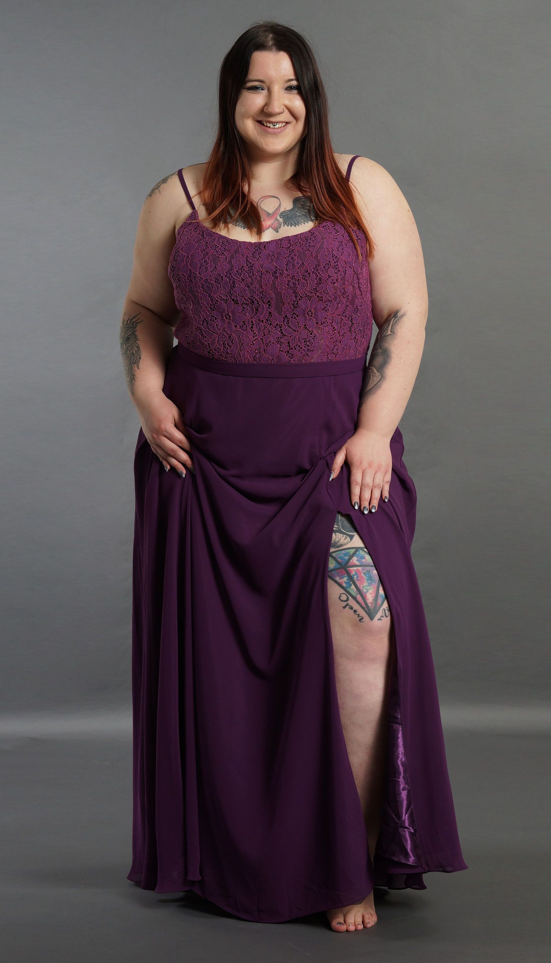 Eine Frau mit Übergröße steht in einem lila Kleid da.