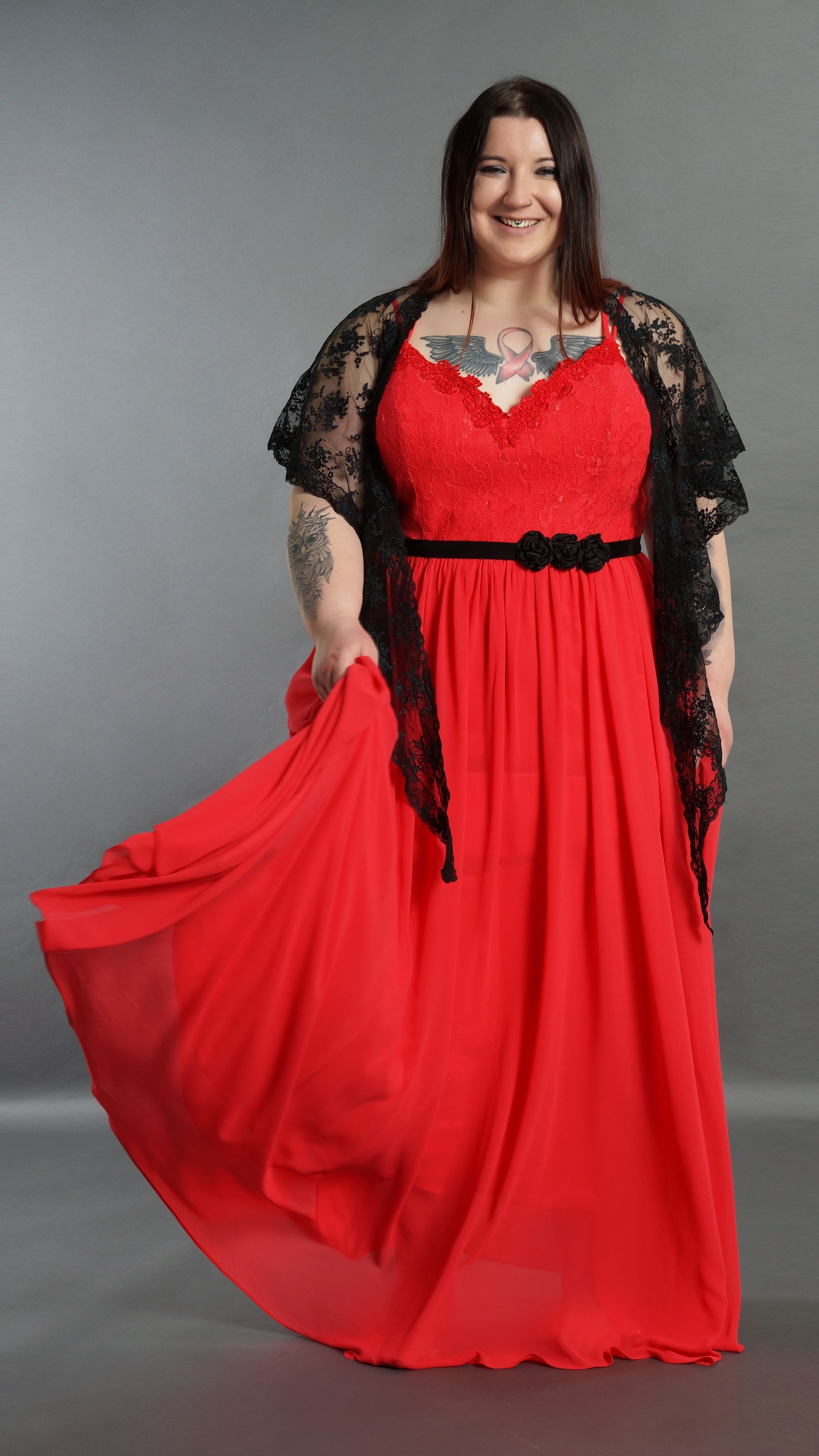 Eine Frau mit Übergröße trägt ein rotes Kleid und eine schwarze Spitzenjacke.