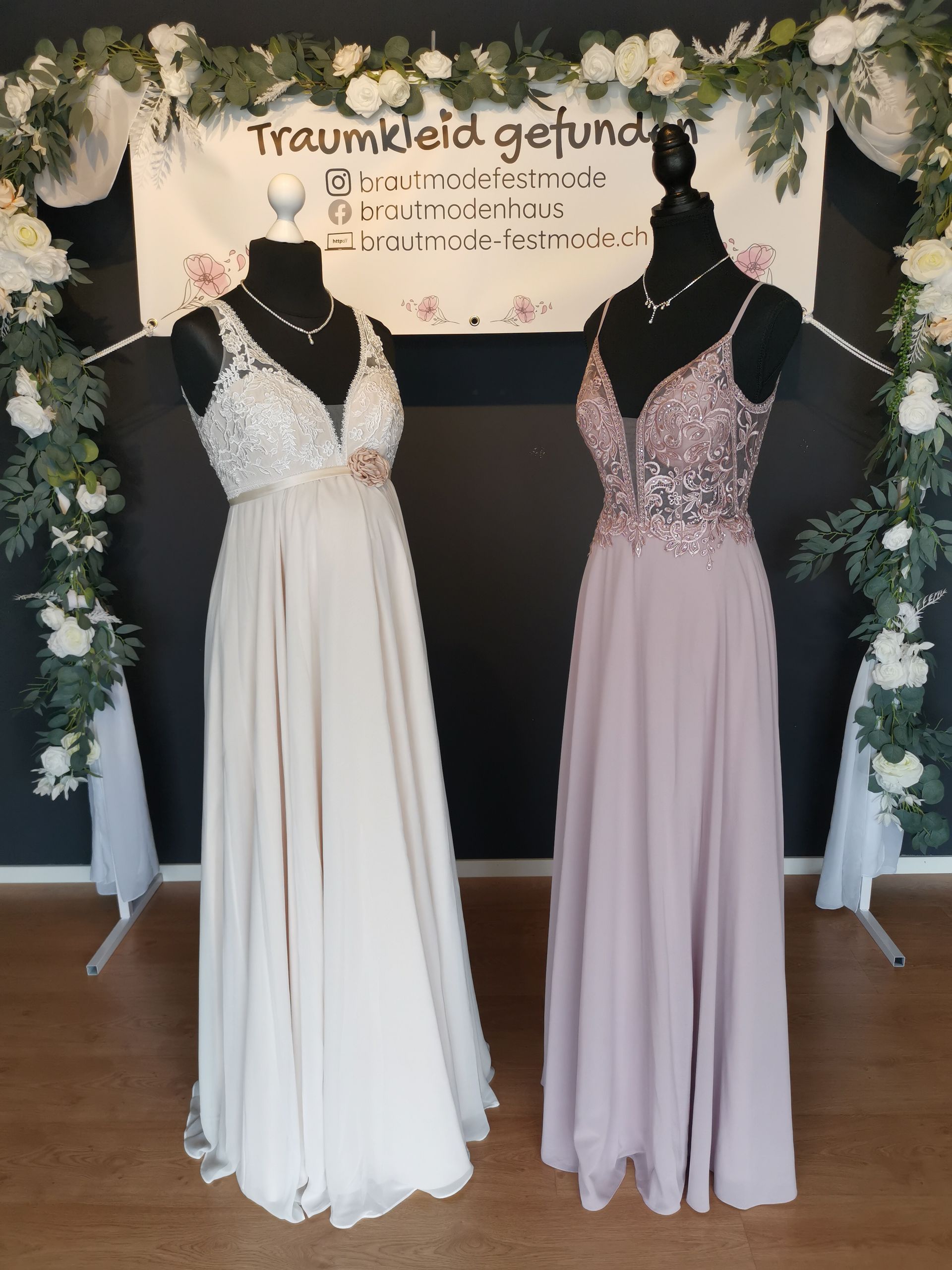 Zwei Schaufensterpuppen in Kleidern stehen nebeneinander vor einem Schild.