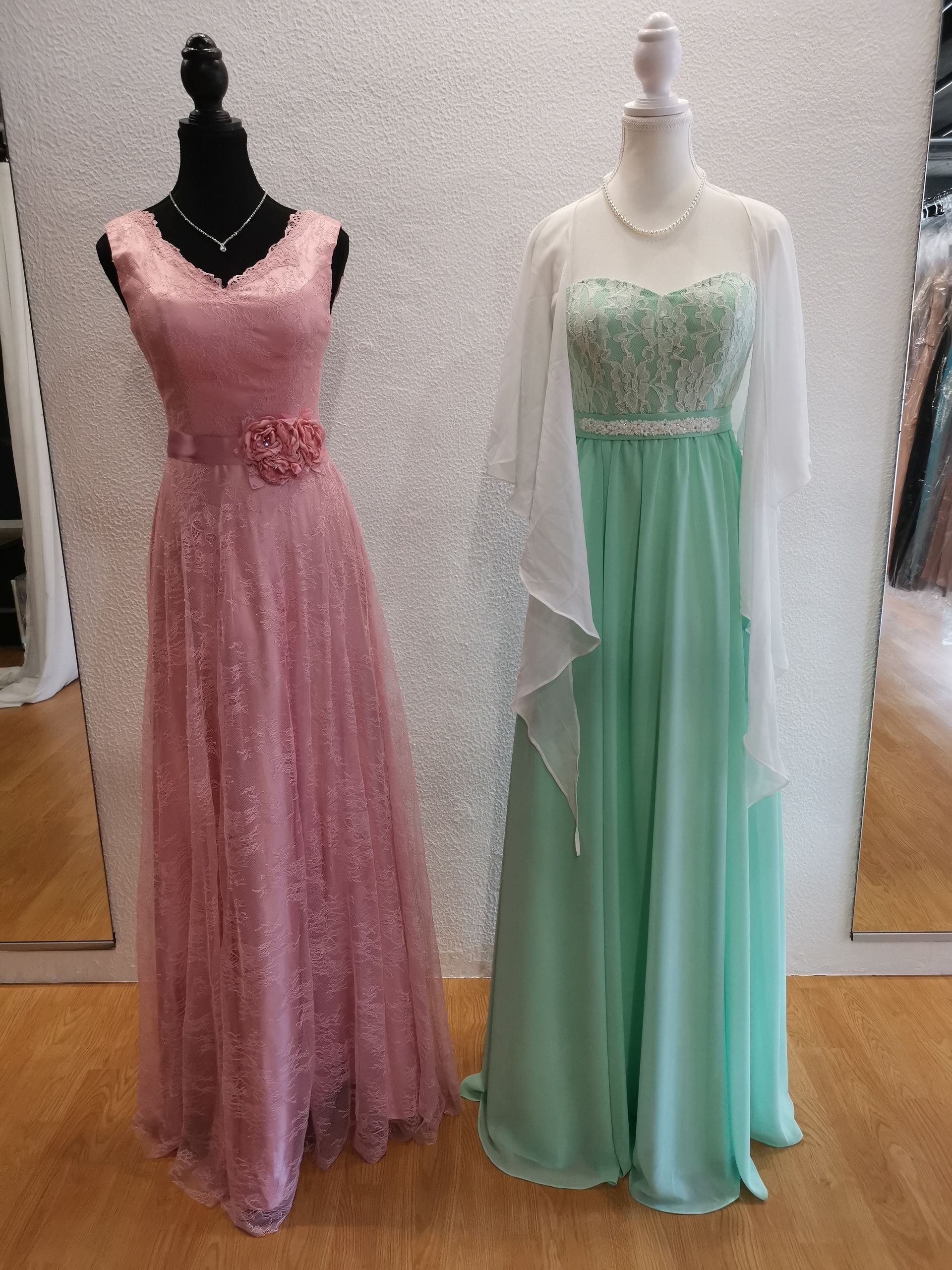 Zwei Kleider hängen an Schaufensterpuppen vor einem Spiegel.