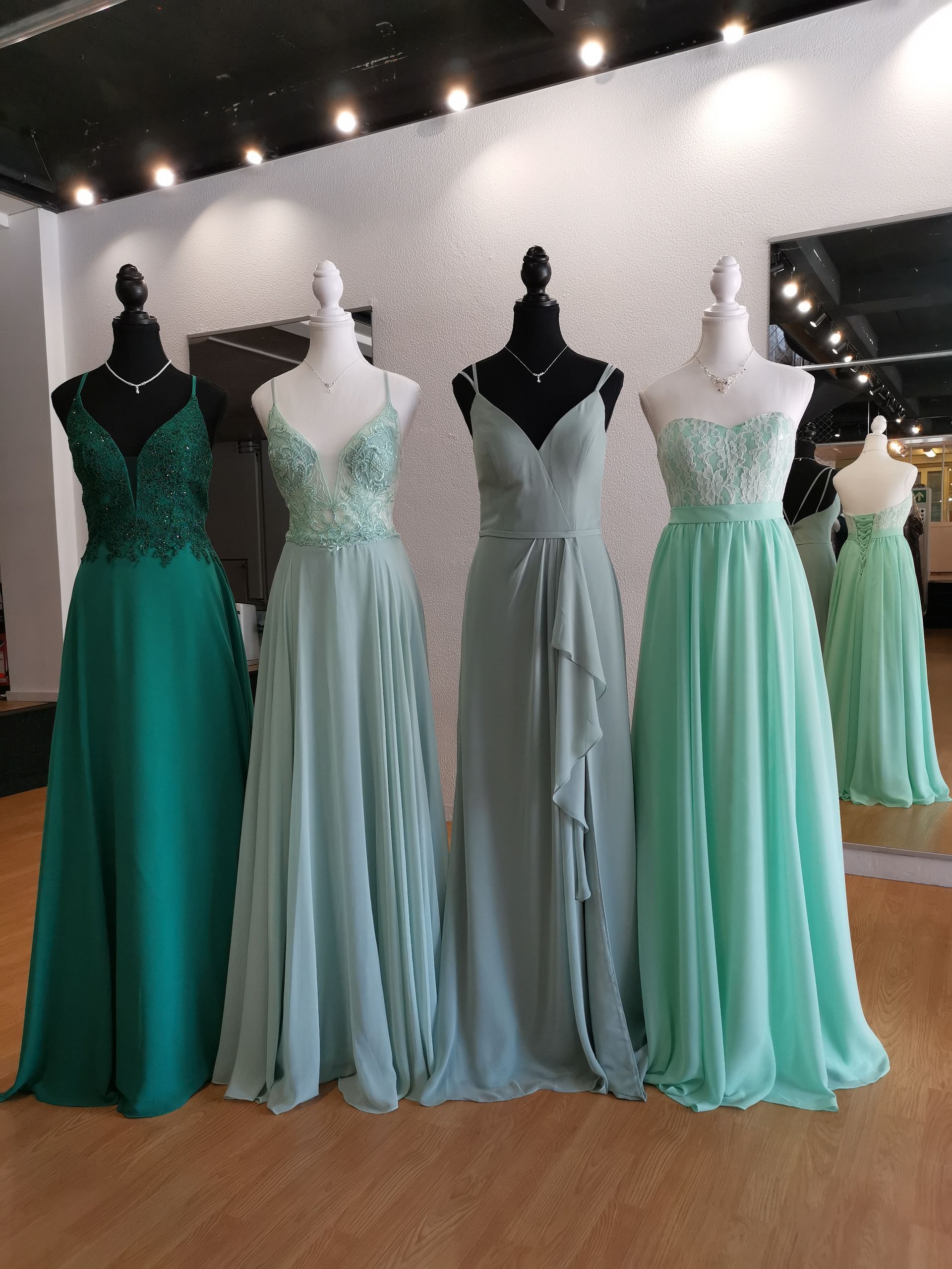 In einem Geschäft sind mehrere grüne Kleider auf Schaufensterpuppen aufgereiht.