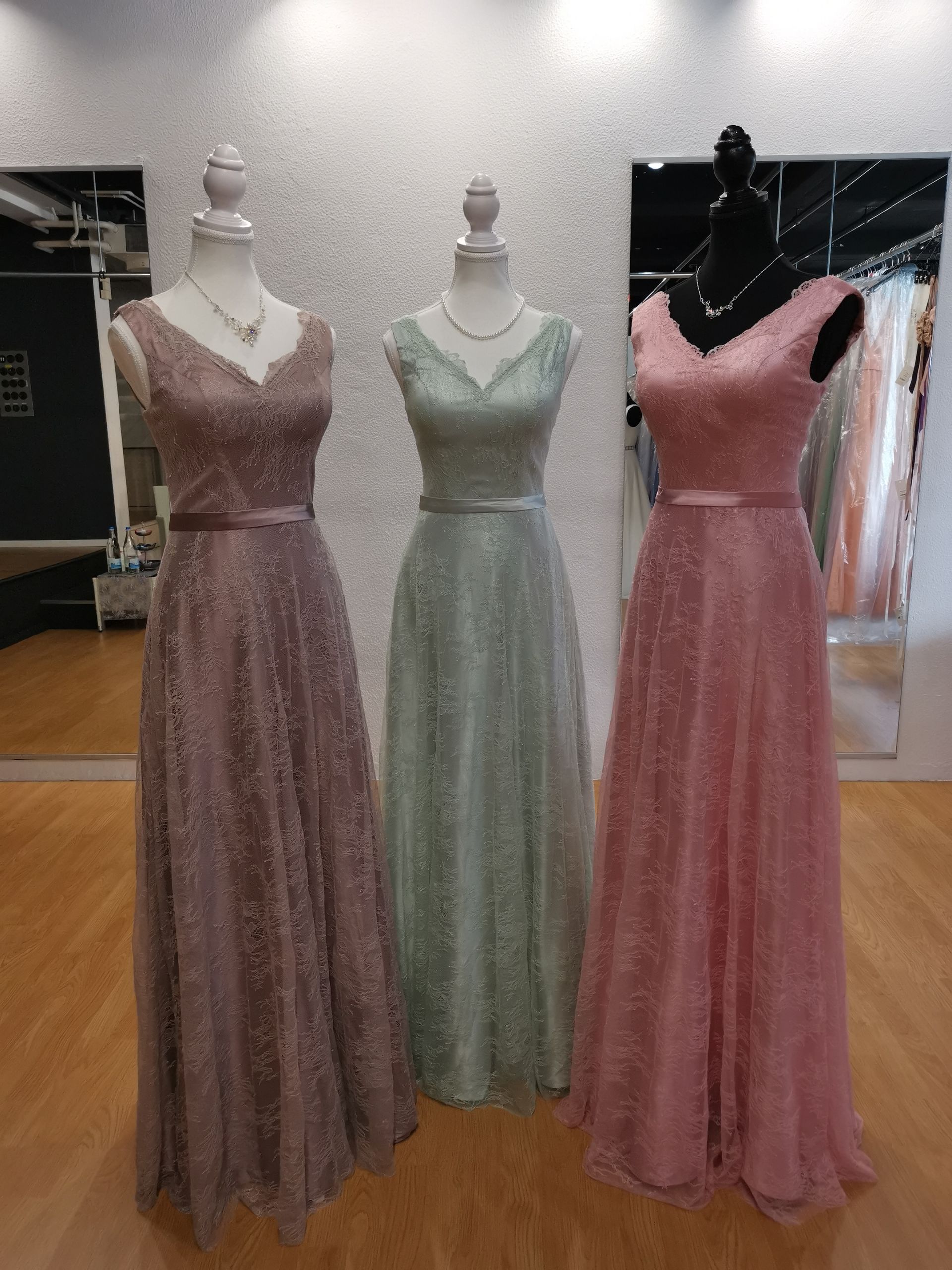 In einem Geschäft hängen drei Kleider an Schaufensterpuppen.