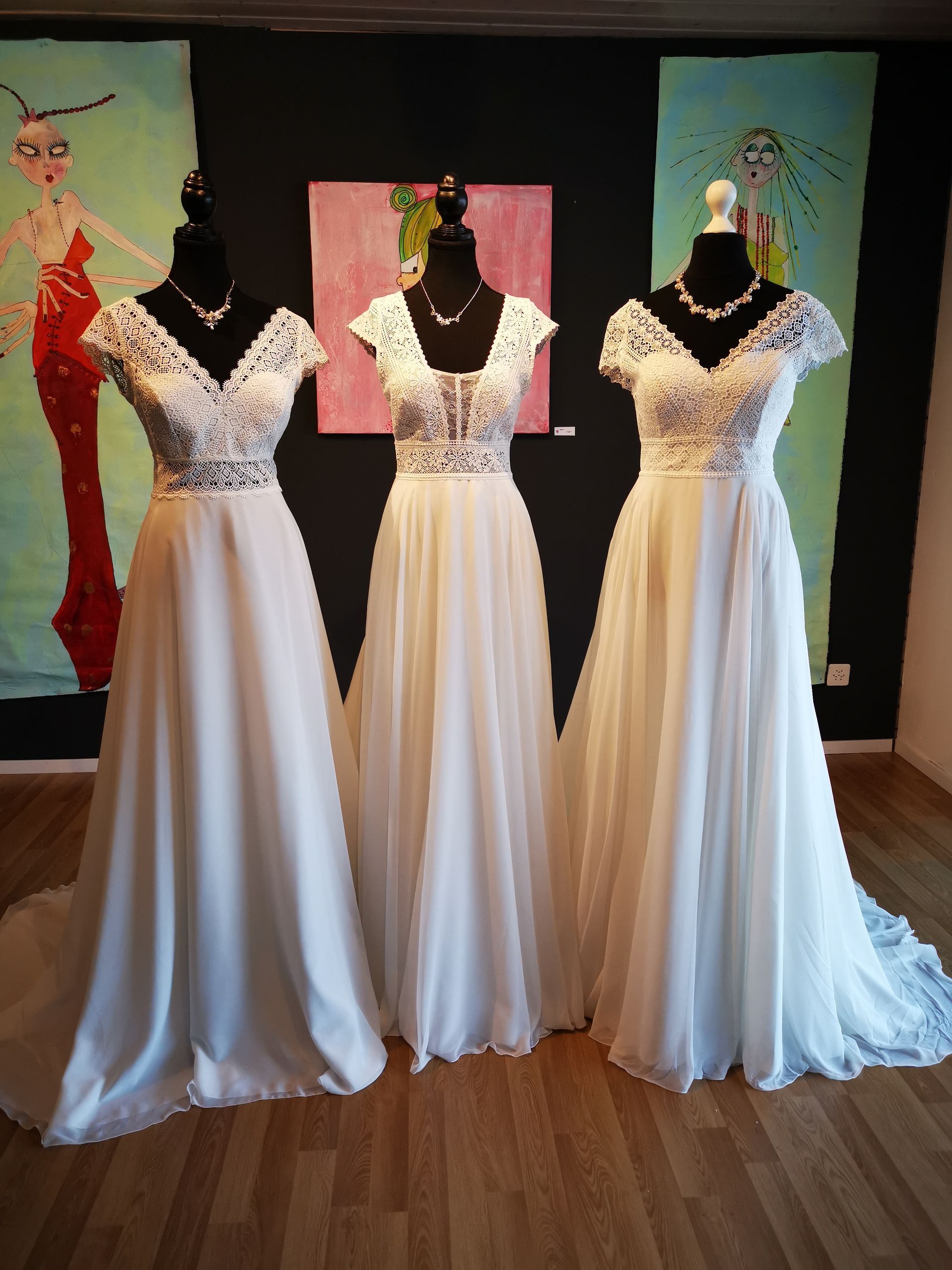 In einem Raum sind drei weiße Brautkleider auf Schaufensterpuppen ausgestellt.