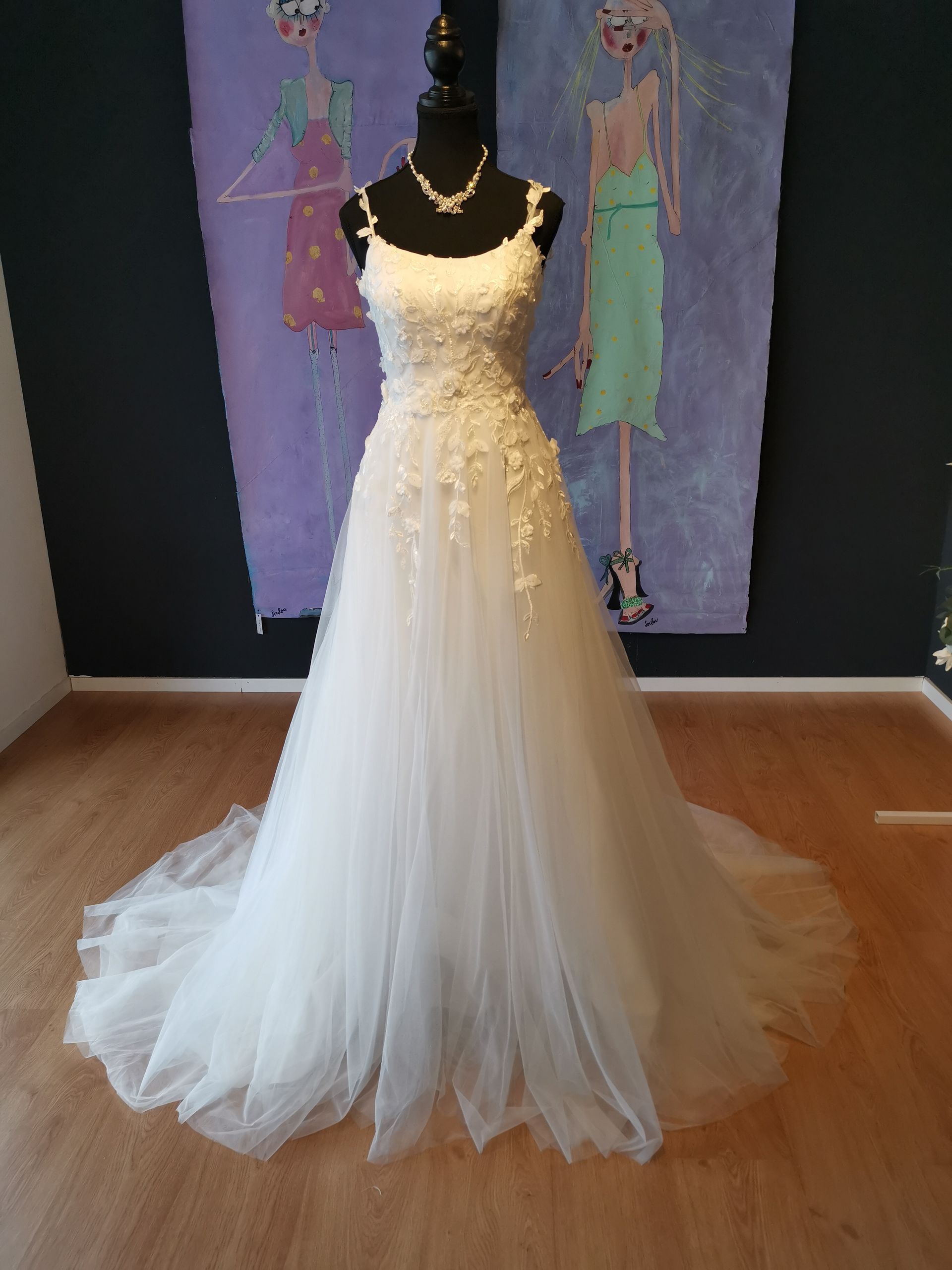 Vor einem Gemälde hängt an einer Schaufensterpuppe ein weißes Brautkleid.