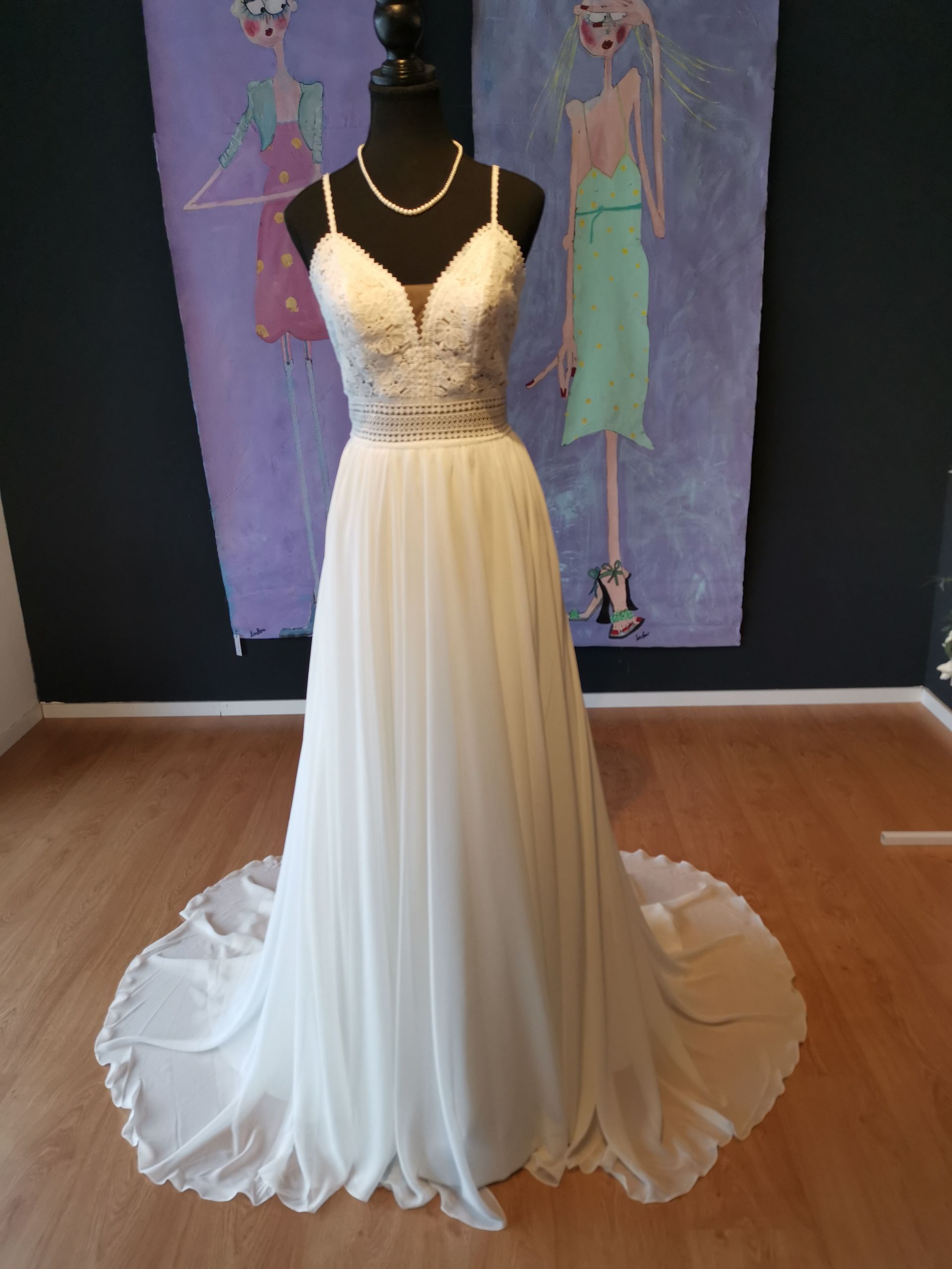 Ein weißes Brautkleid hängt an einer Schaufensterpuppe vor einem Gemälde