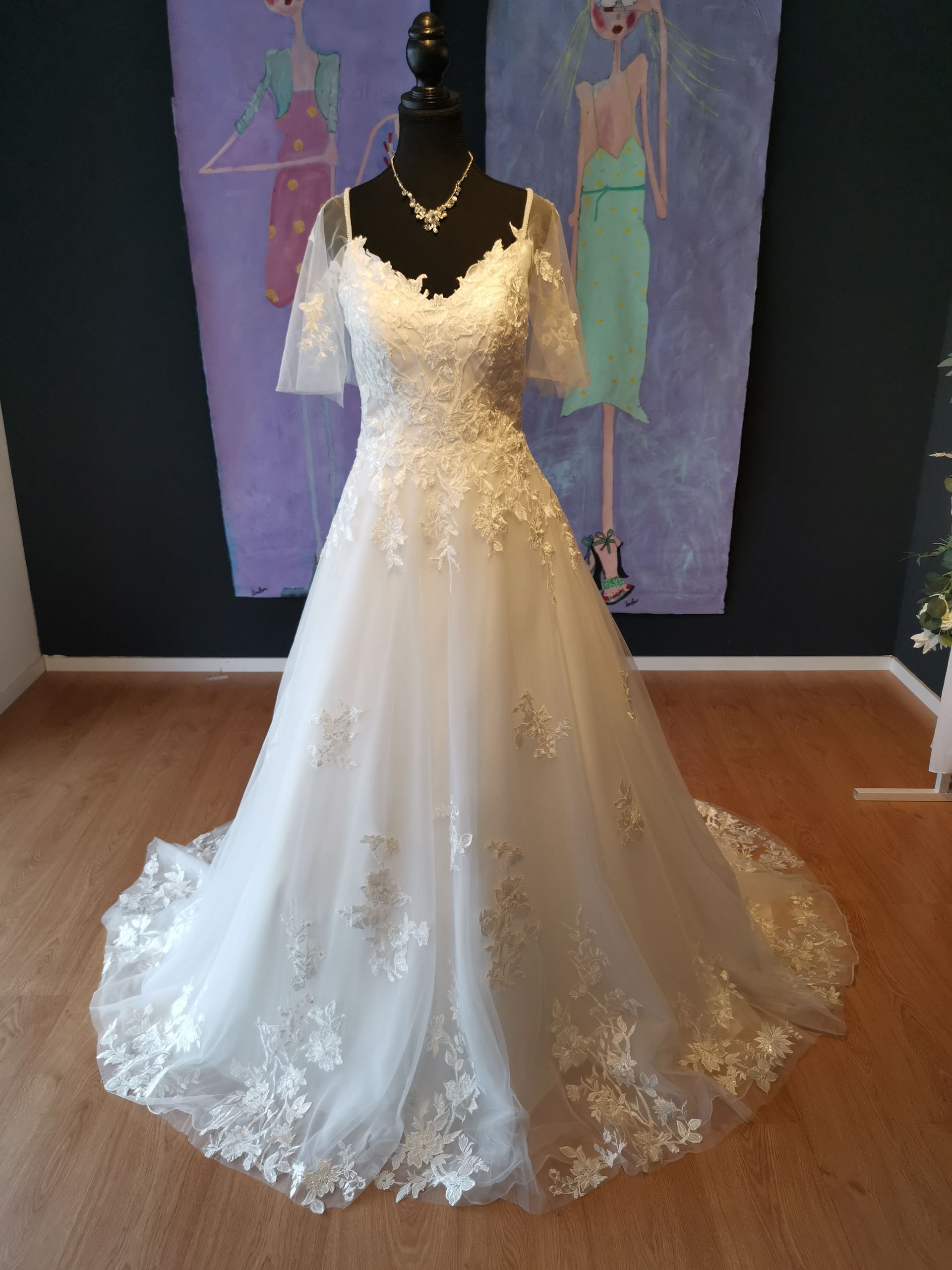 Ein weißes Brautkleid hängt an einer Schaufensterpuppe vor einem Gemälde