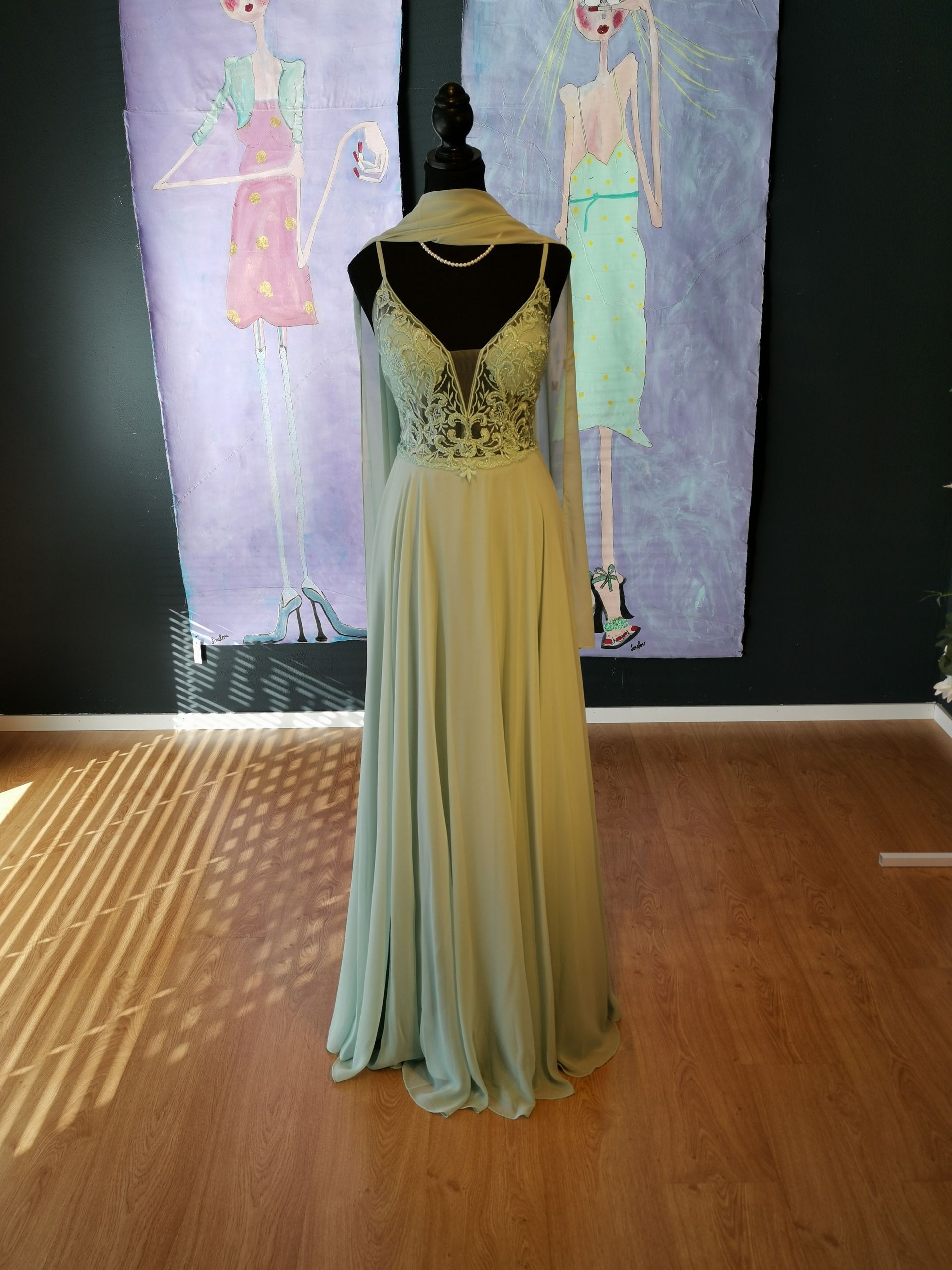 Ein grünes Kleid hängt an einer Schaufensterpuppe vor zwei Gemälden