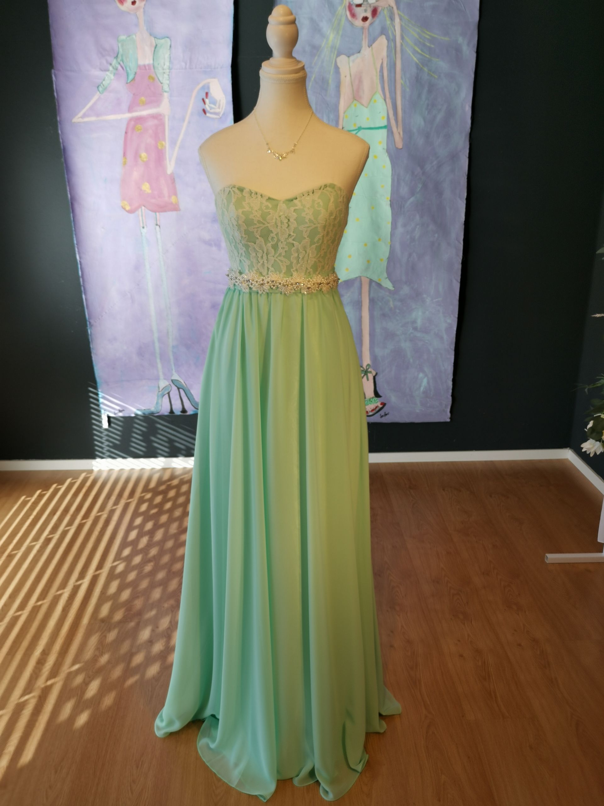 Ein grünes Kleid hängt an einer Schaufensterpuppe vor einem Gemälde