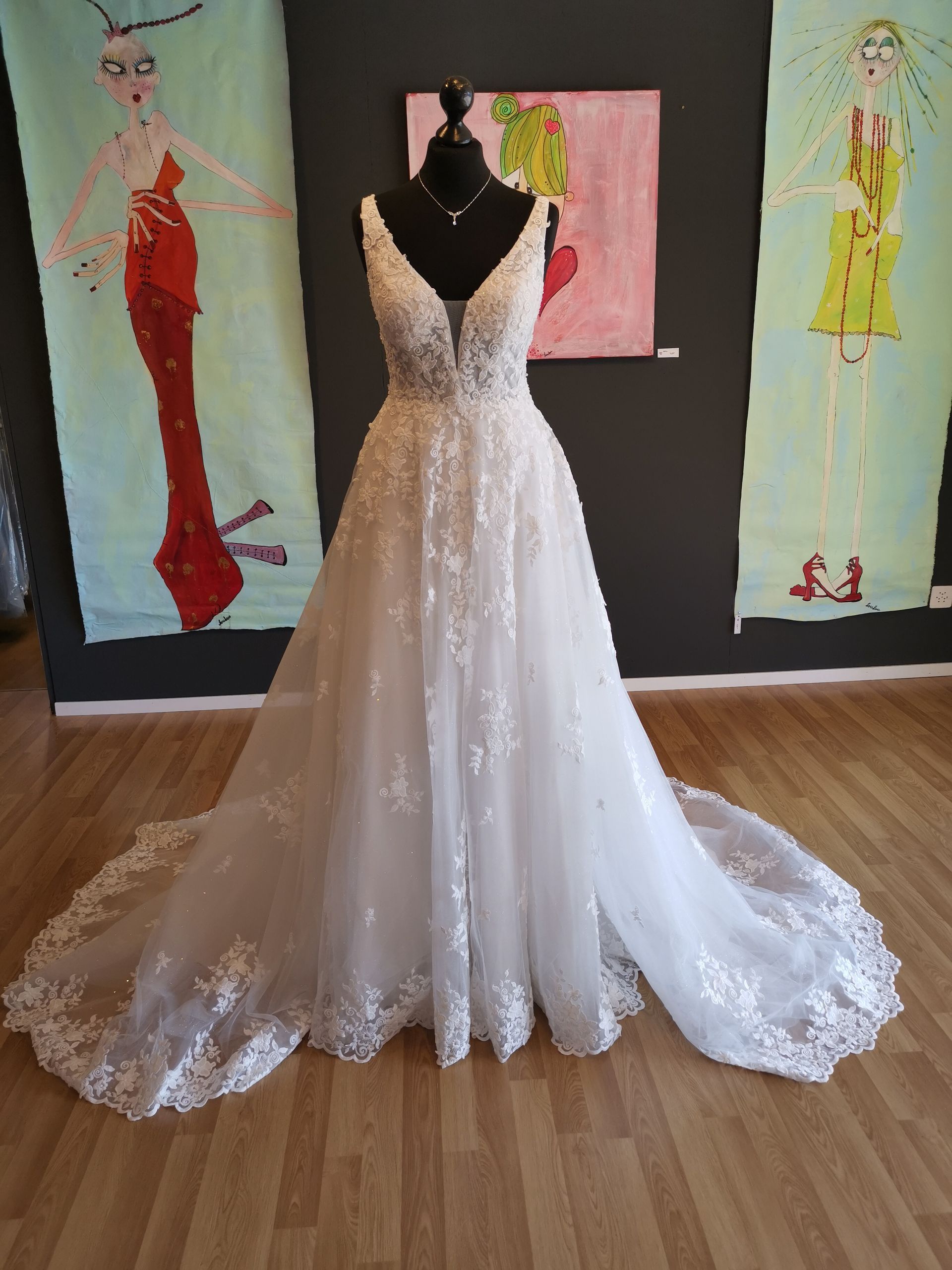 Vor drei Gemälden hängt an einer Schaufensterpuppe ein weißes Brautkleid.