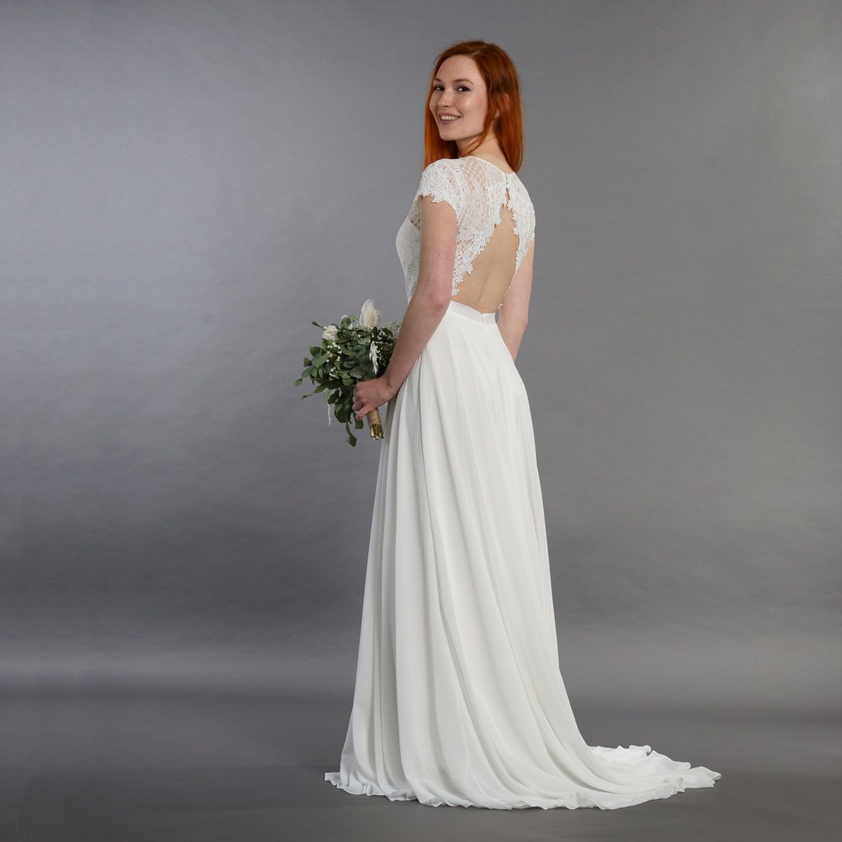 Eine Frau in einem weißen Brautkleid hält einen Blumenstrauß.