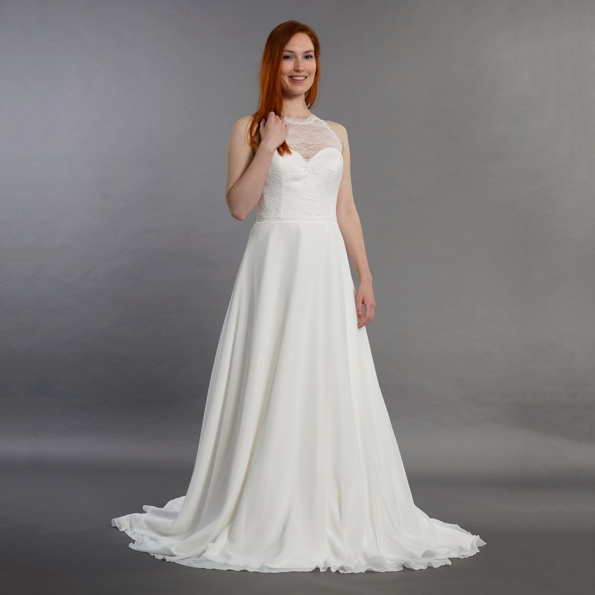 Eine Frau in einem weißen Brautkleid steht vor einem grauen Hintergrund