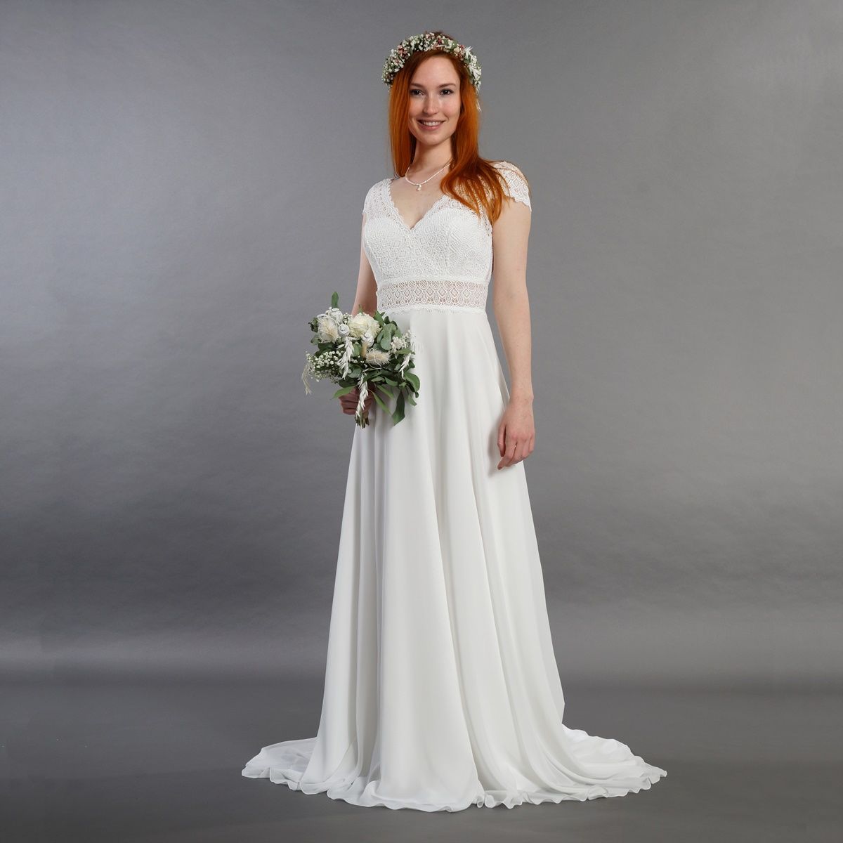 Eine Frau in einem weißen Brautkleid hält einen Blumenstrauß.