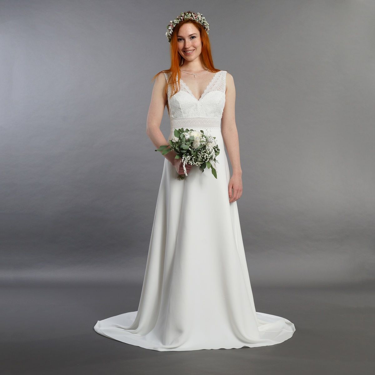 Eine Frau in einem weißen Brautkleid hält einen Blumenstrauß.