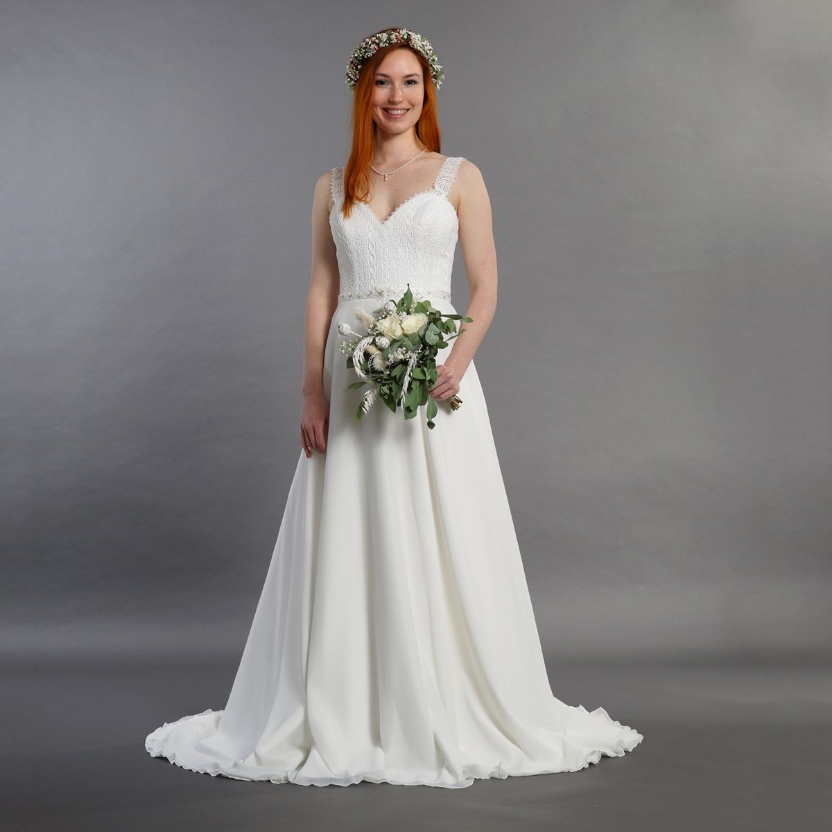 Eine Frau in einem weißen Brautkleid hält einen Blumenstrauß.