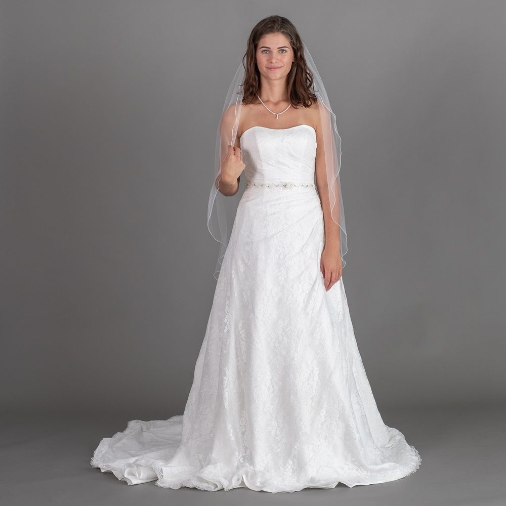 Eine Frau in einem weißen Brautkleid und Schleier steht vor einem grauen Hintergrund.