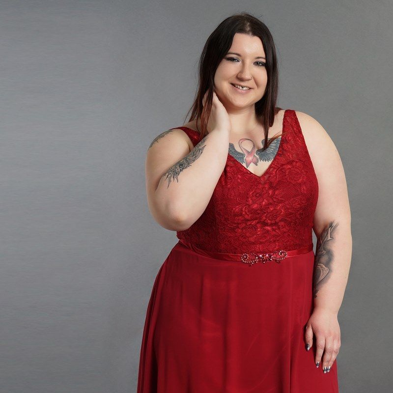 Eine Frau mit einer Tätowierung auf dem Arm trägt ein rotes Kleid