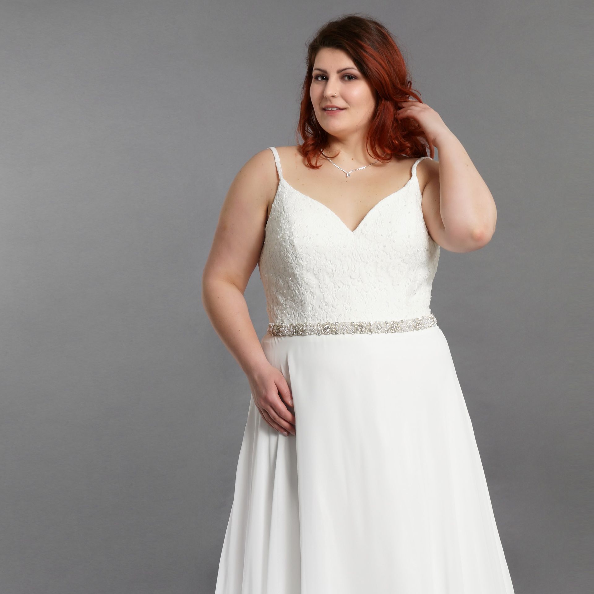 Eine Frau in einem weißen Kleid steht vor einem grauen Hintergrund