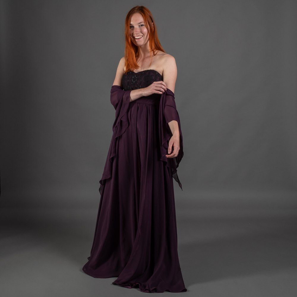 Eine Frau in einem lila Kleid steht vor einem grauen Hintergrund.