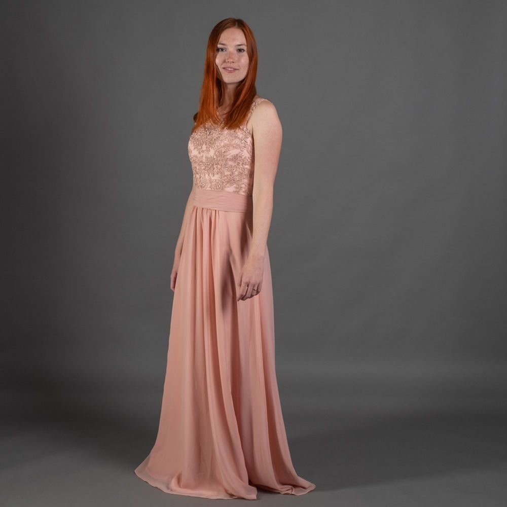 Eine Frau in einem langen rosa Kleid steht vor einem grauen Hintergrund.