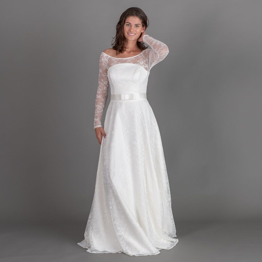 Eine Frau trägt ein weißes Spitzenbrautkleid mit langen Ärmeln.