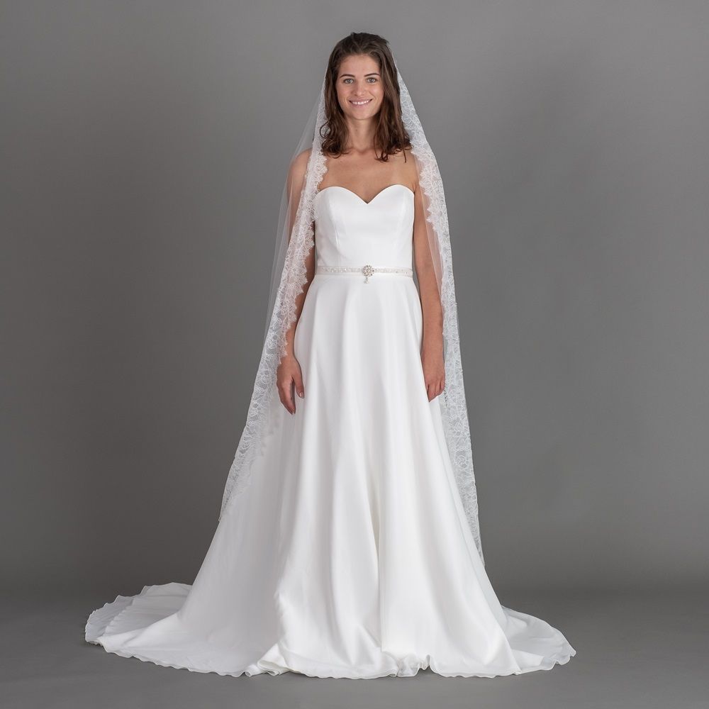 Eine Frau in einem weißen Brautkleid und Schleier steht vor einem grauen Hintergrund.