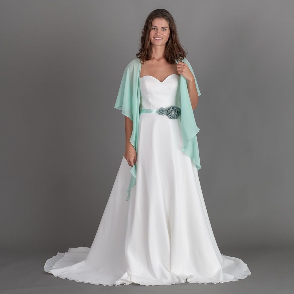 Eine Frau in einem weißen Brautkleid trägt einen grünen Schal