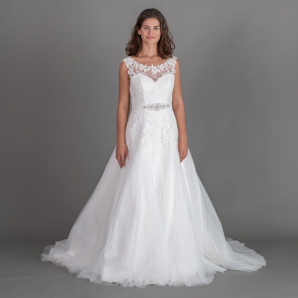 Eine Frau in einem weißen Brautkleid steht vor einem grauen Hintergrund.