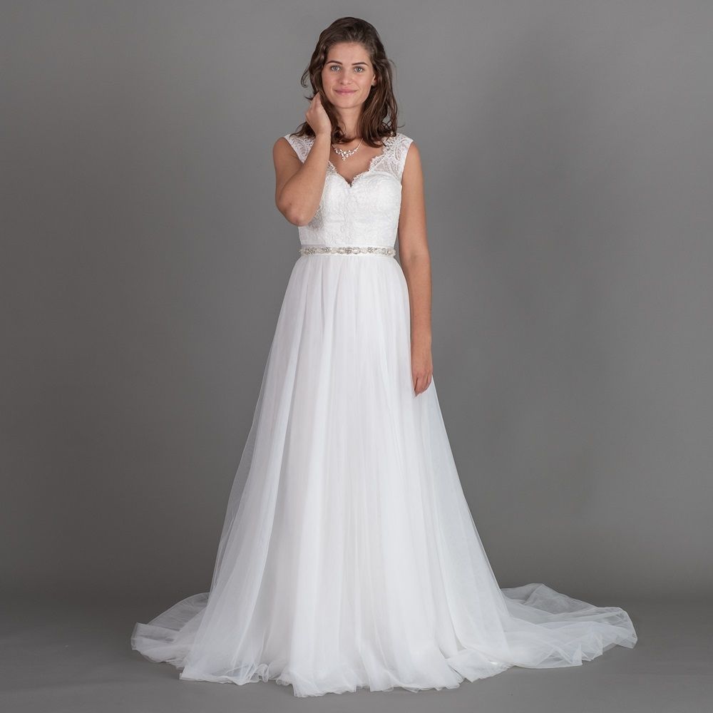 Eine Frau in einem weißen Brautkleid steht vor einem grauen Hintergrund.