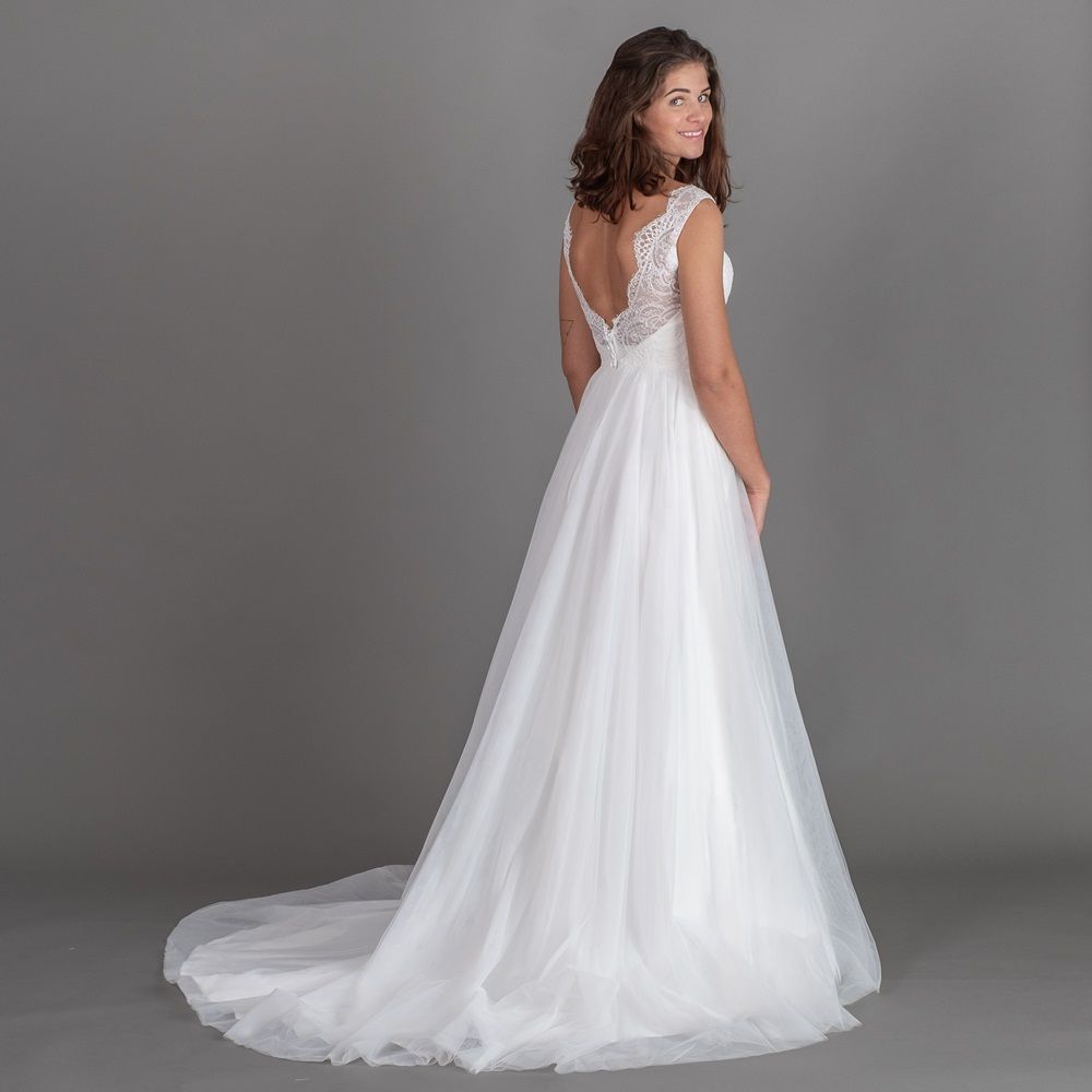 Eine Frau in einem weißen Brautkleid steht vor einem grauen Hintergrund.