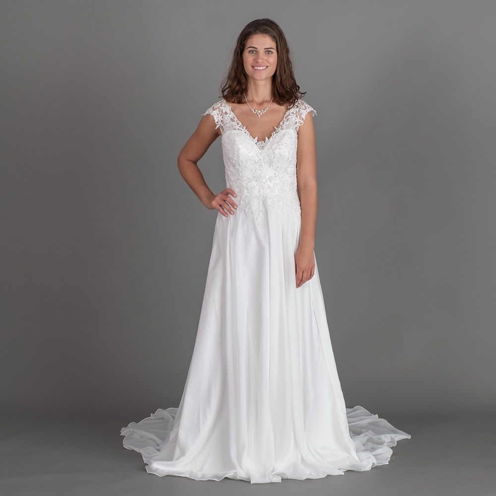 Eine Frau in einem weißen Brautkleid steht vor einem grauen Hintergrund.